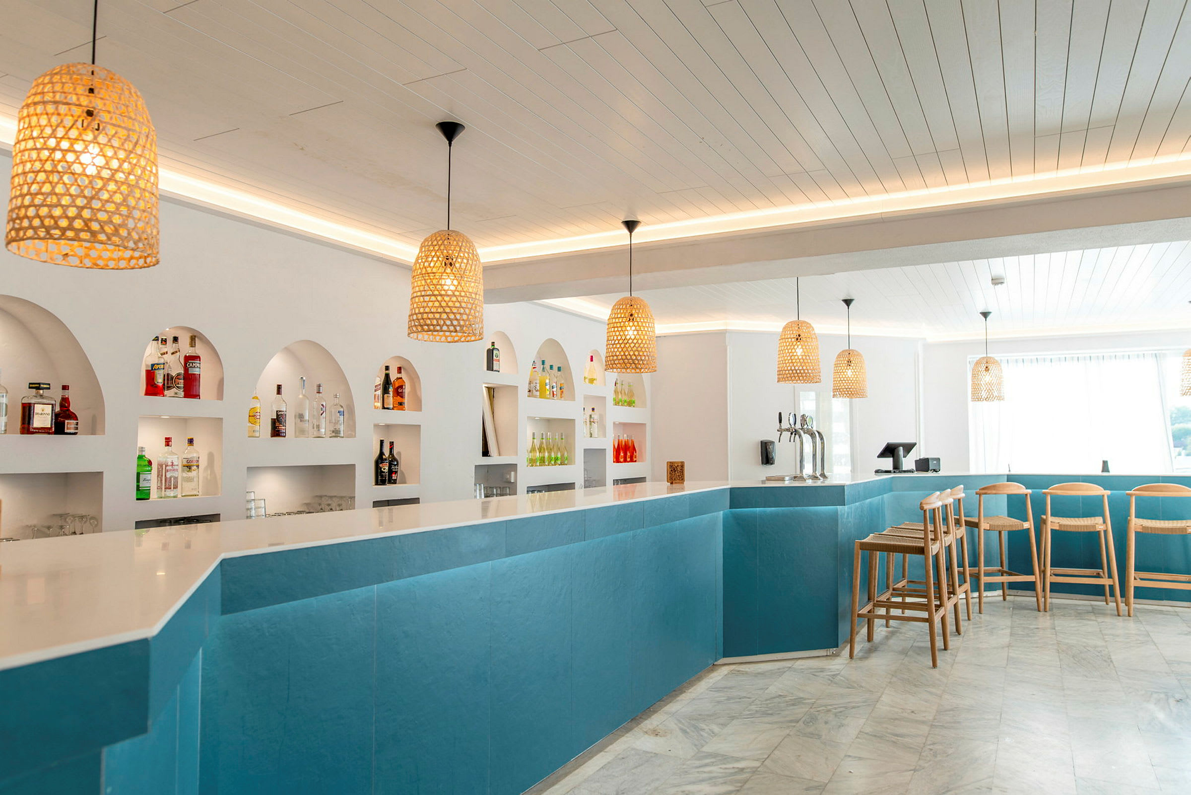 En moderne bar med blå paneler, hvid bordplade og flere flasker på hylder bagved. (AI-genereret tekst)