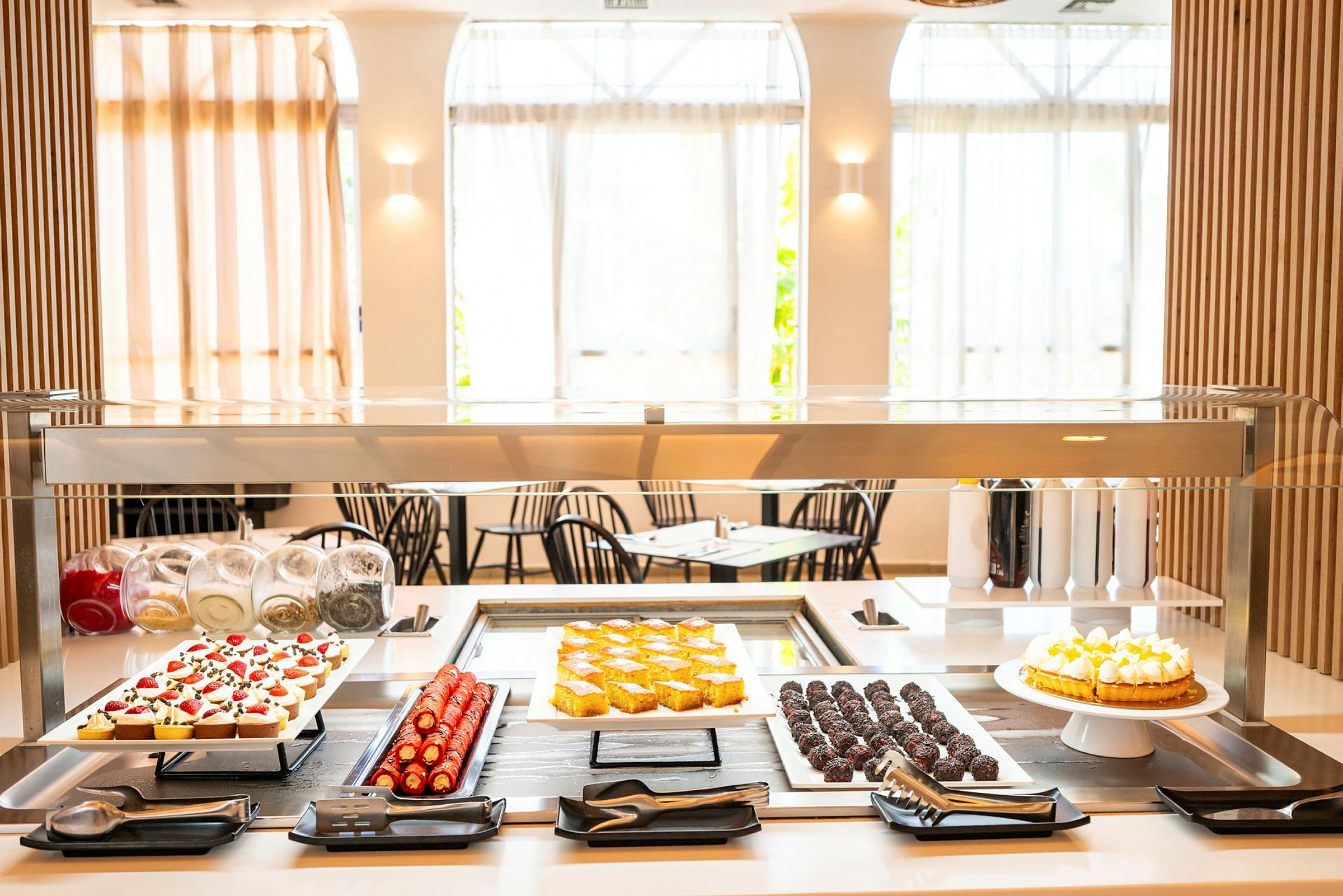 Et dessertbord med forskellige bagværk og kager under en glasbeskyttelse. (AI-genereret tekst)