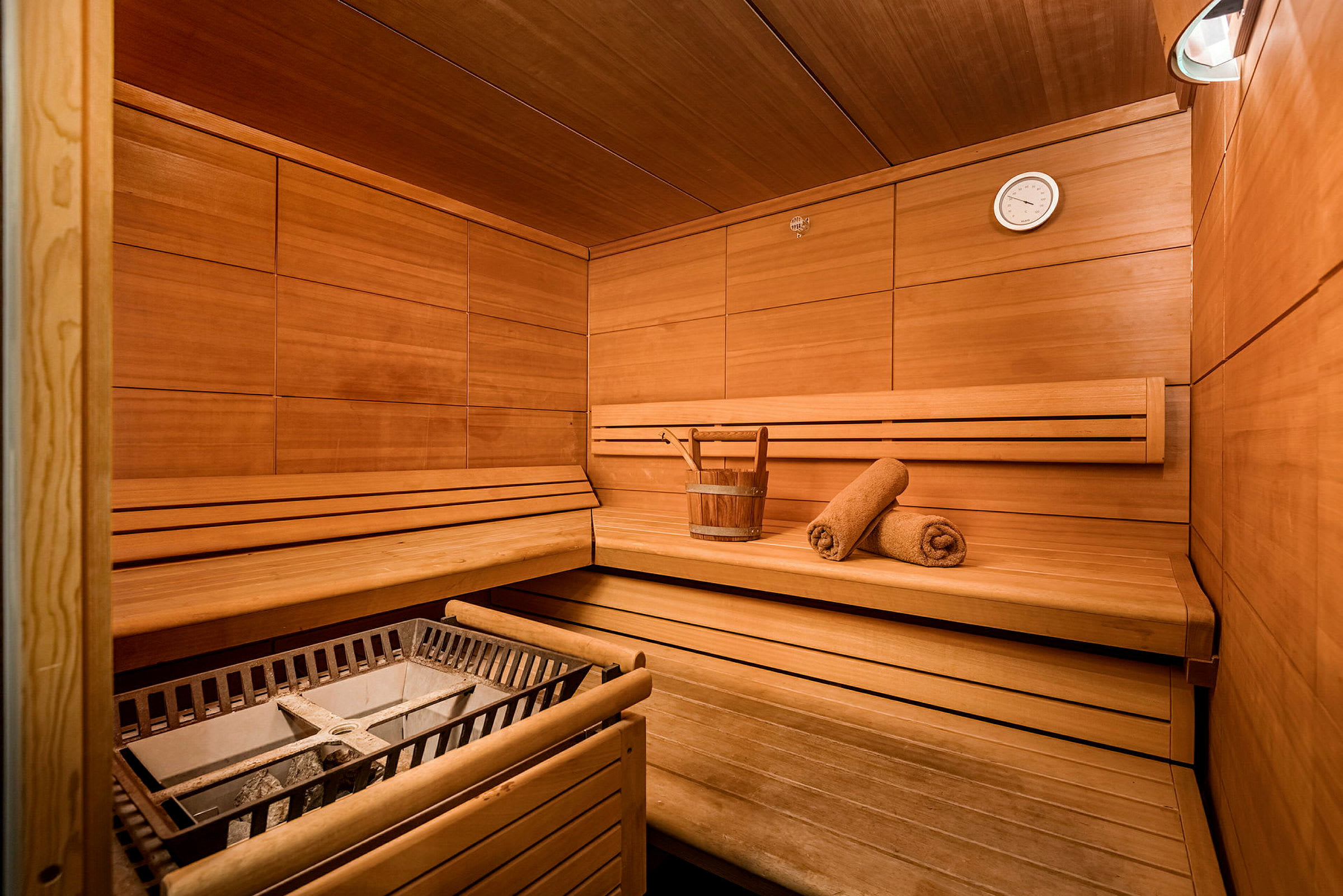 En træbeklædt sauna med siddepladser, en spand og to håndklæder. (AI-genereret tekst)
