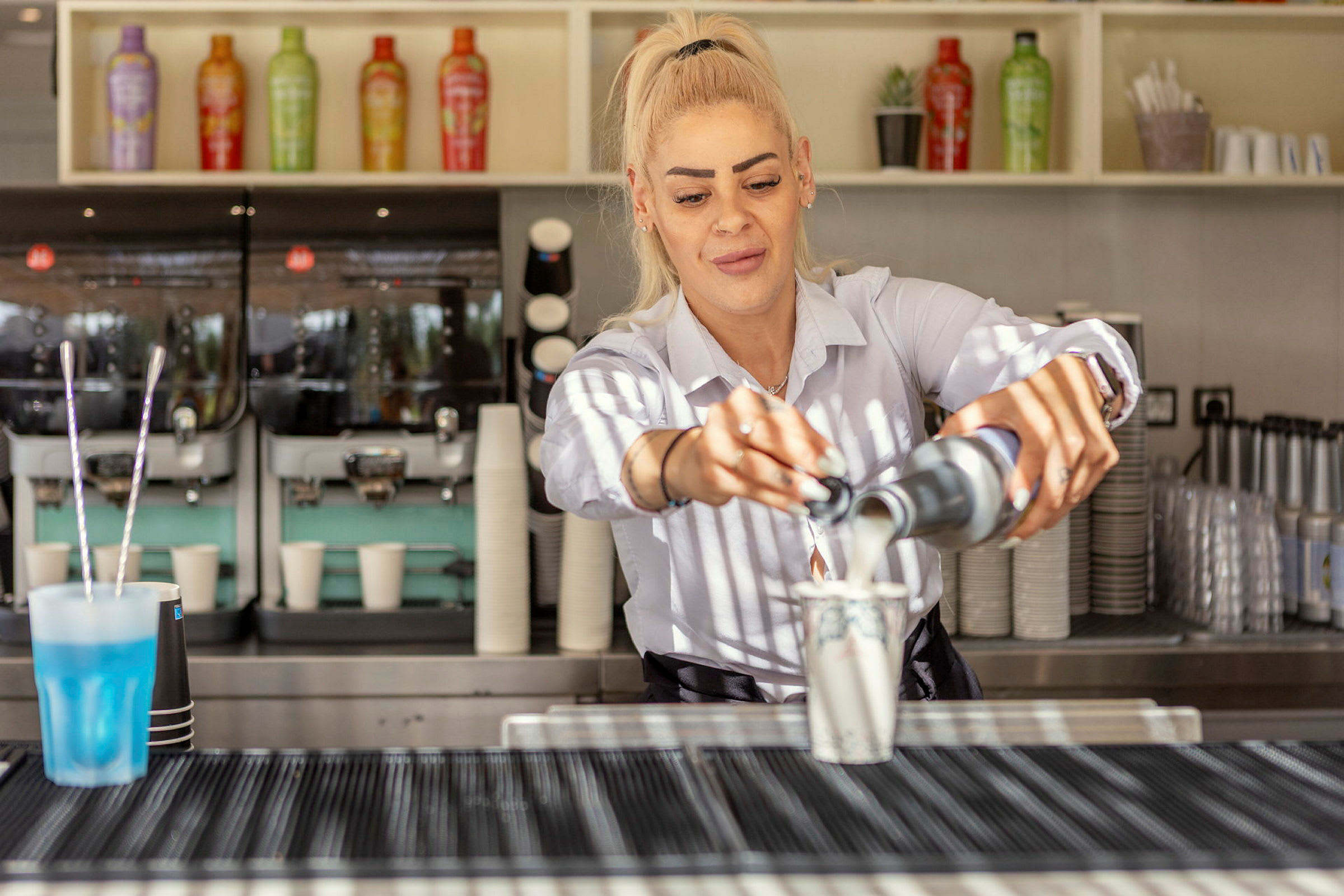 Person hælder en væske i en kop bag en kaffebar. (AI-genereret tekst)