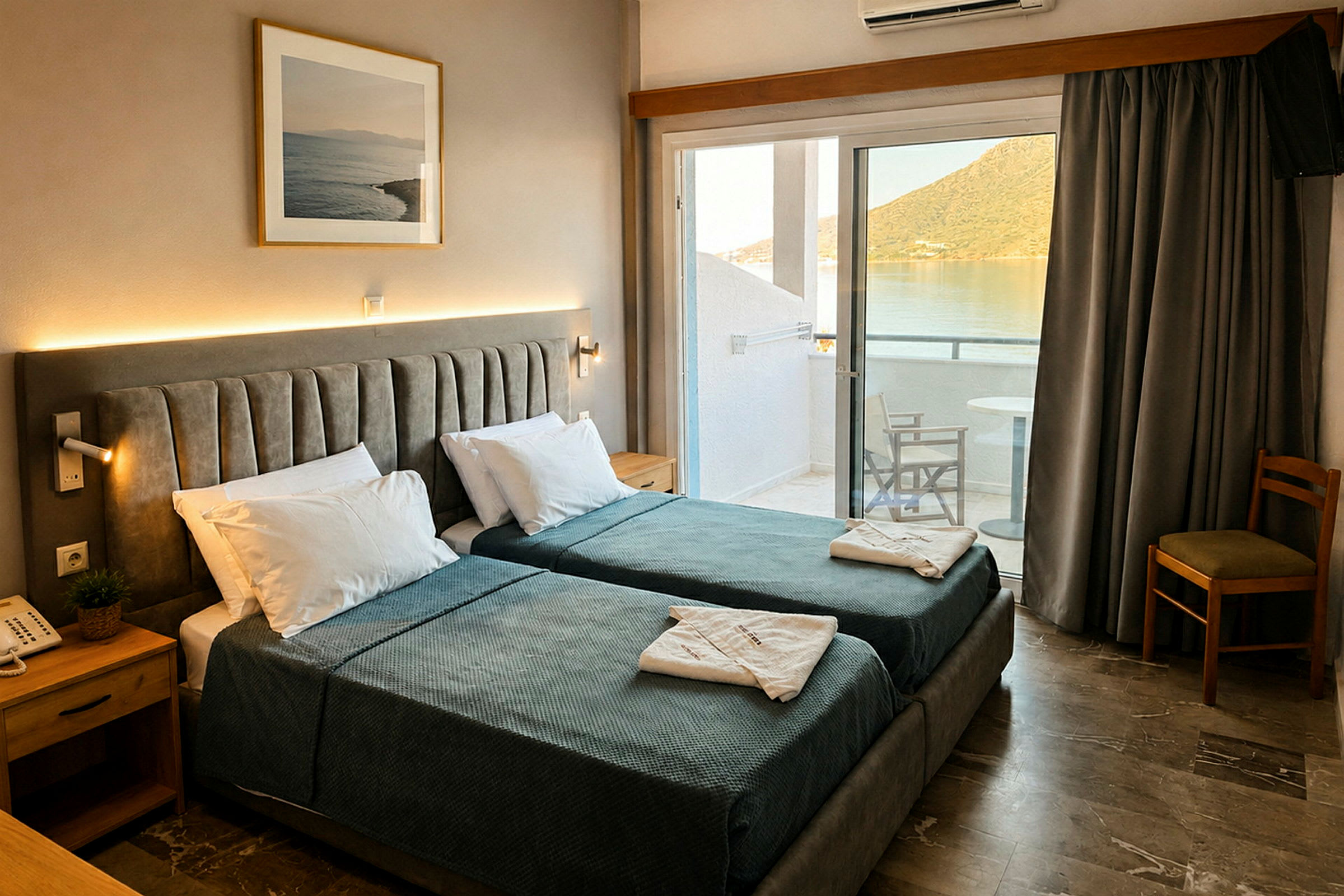 Hotelværelse med to enkeltsenge, natbord og billede på væggen. Altan med udsigt over vand og bjerge. (AI-genereret tekst)