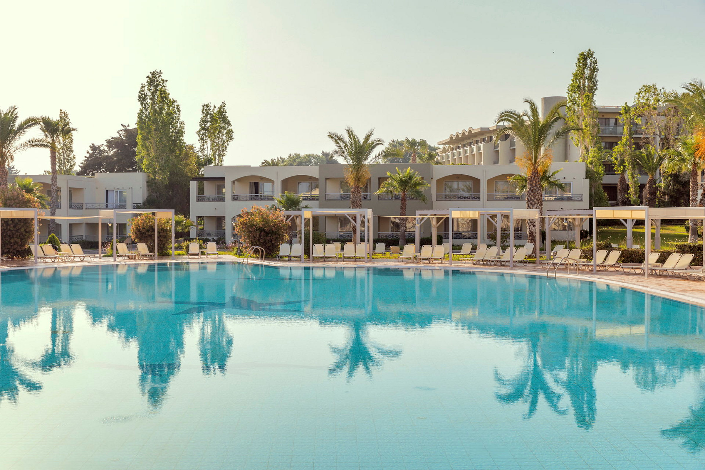 En udendørs pool foran hotelbygninger og palmer. (AI-genereret tekst)