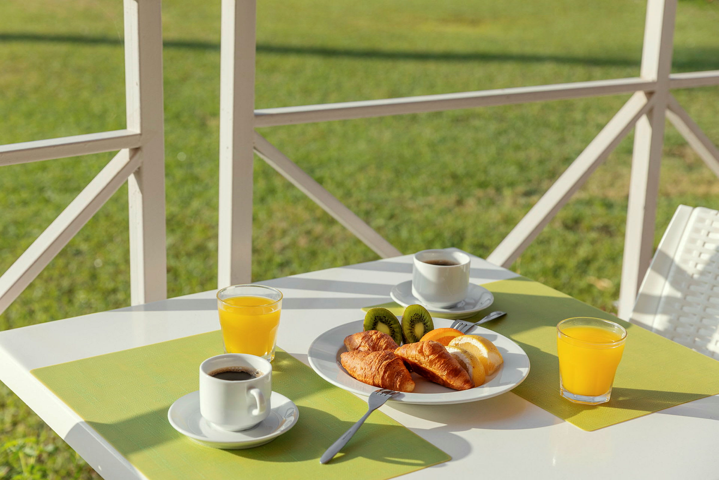 Morgenmad med kaffe, juice, croissanter og kiwi på et hvidt bord med grøn borddug. (AI-genereret tekst)