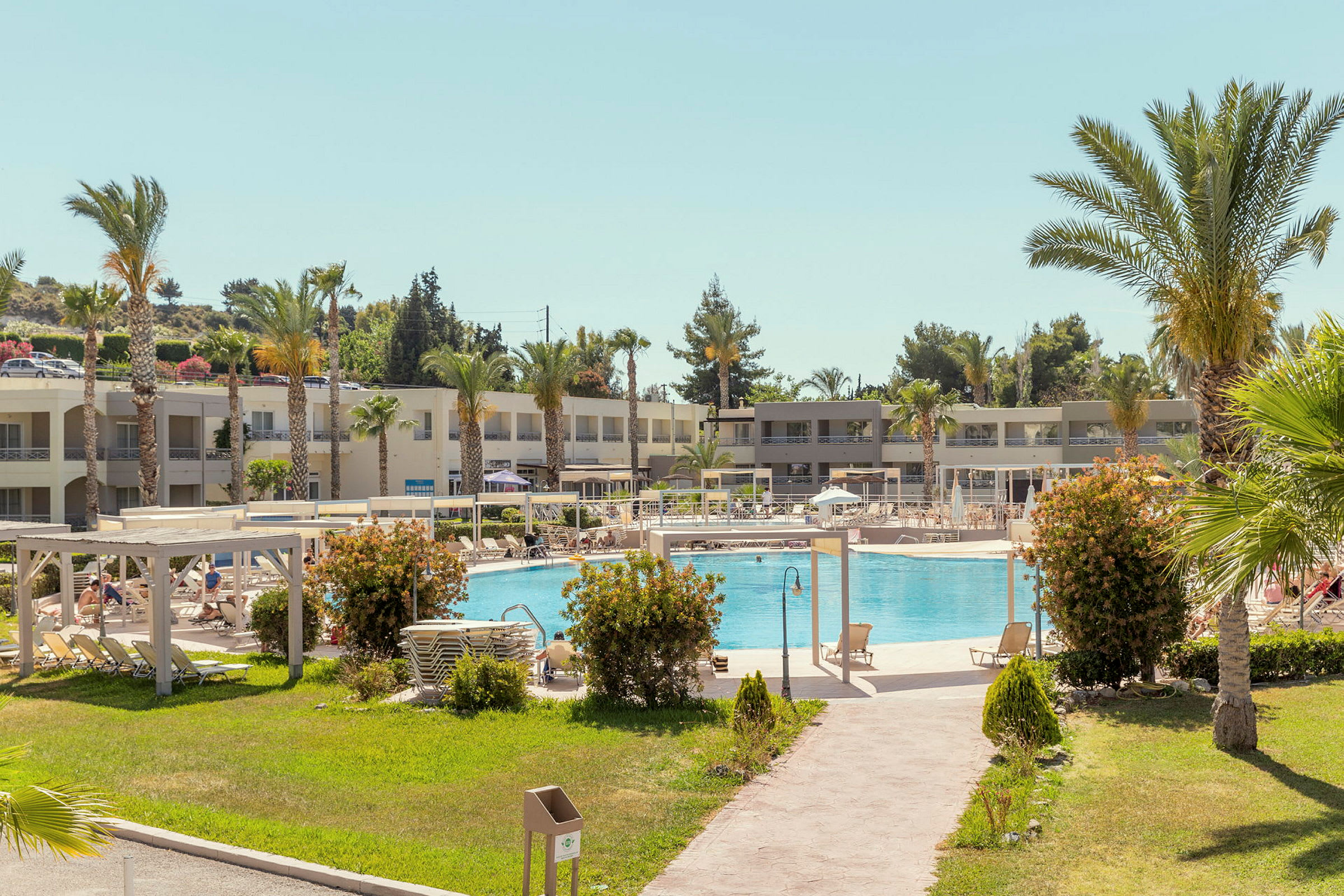Hotelanlæg med pool, liggestole og grønt område. (AI-genereret tekst)