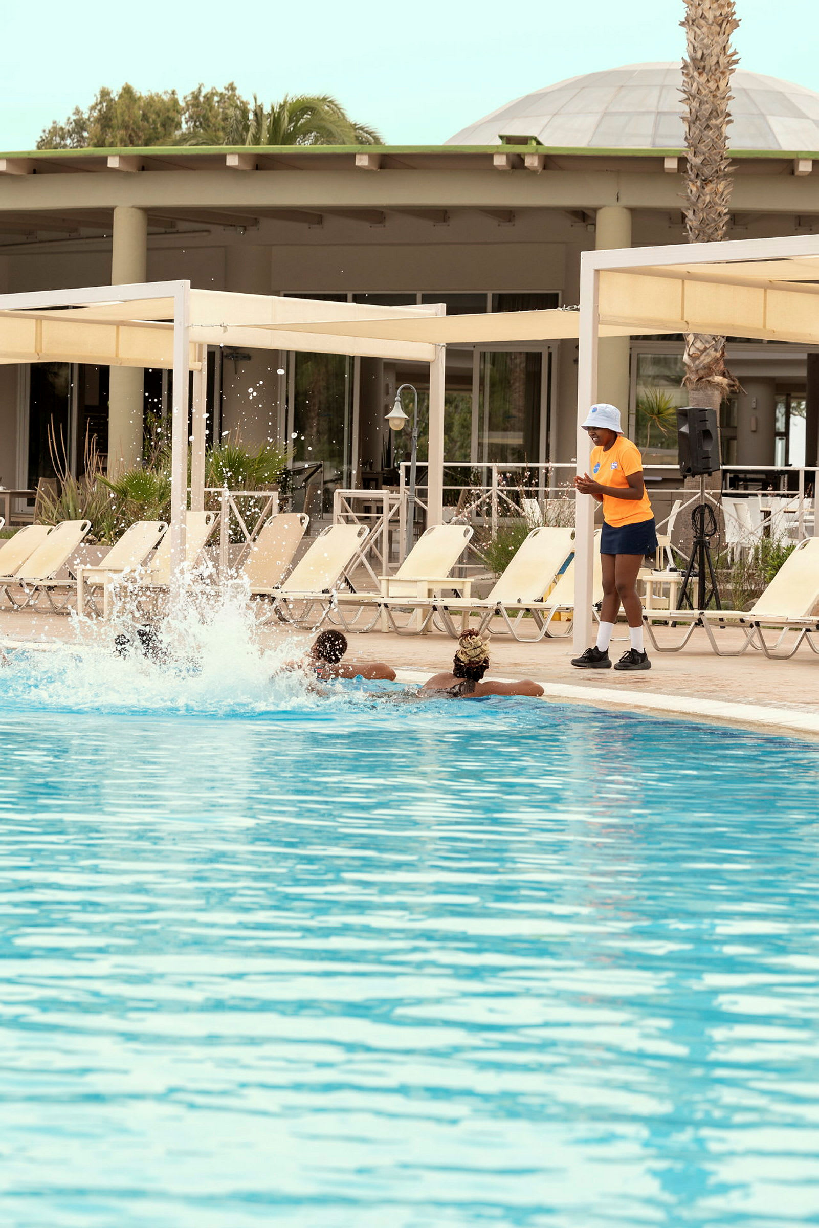 Personer svømmer i en pool nær liggestole og en veranda. (AI-genereret tekst)