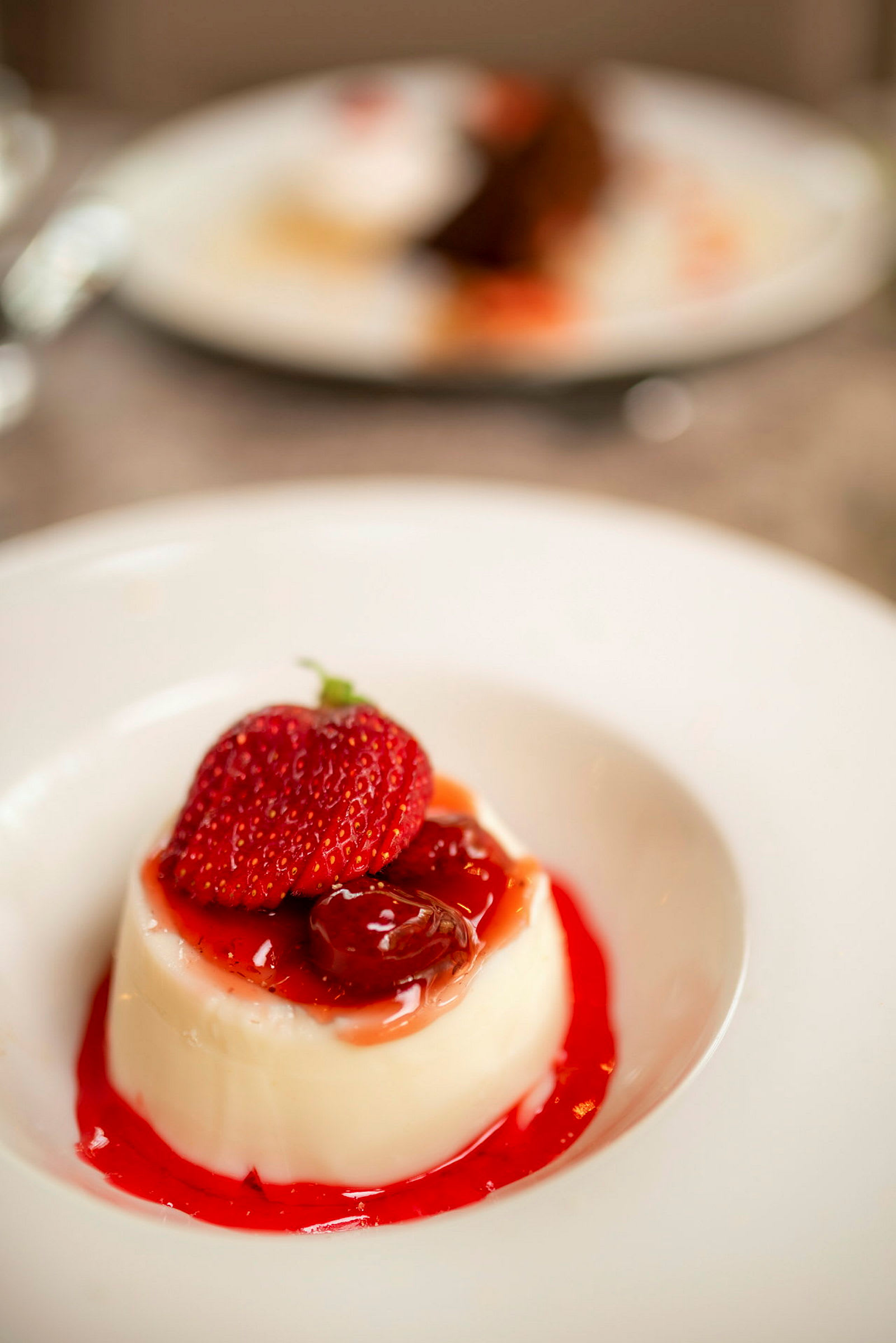 En dessert med vaniljebudding toppet med jordbær og frugt i en rød sauce på en hvid tallerken. (AI-genereret tekst)