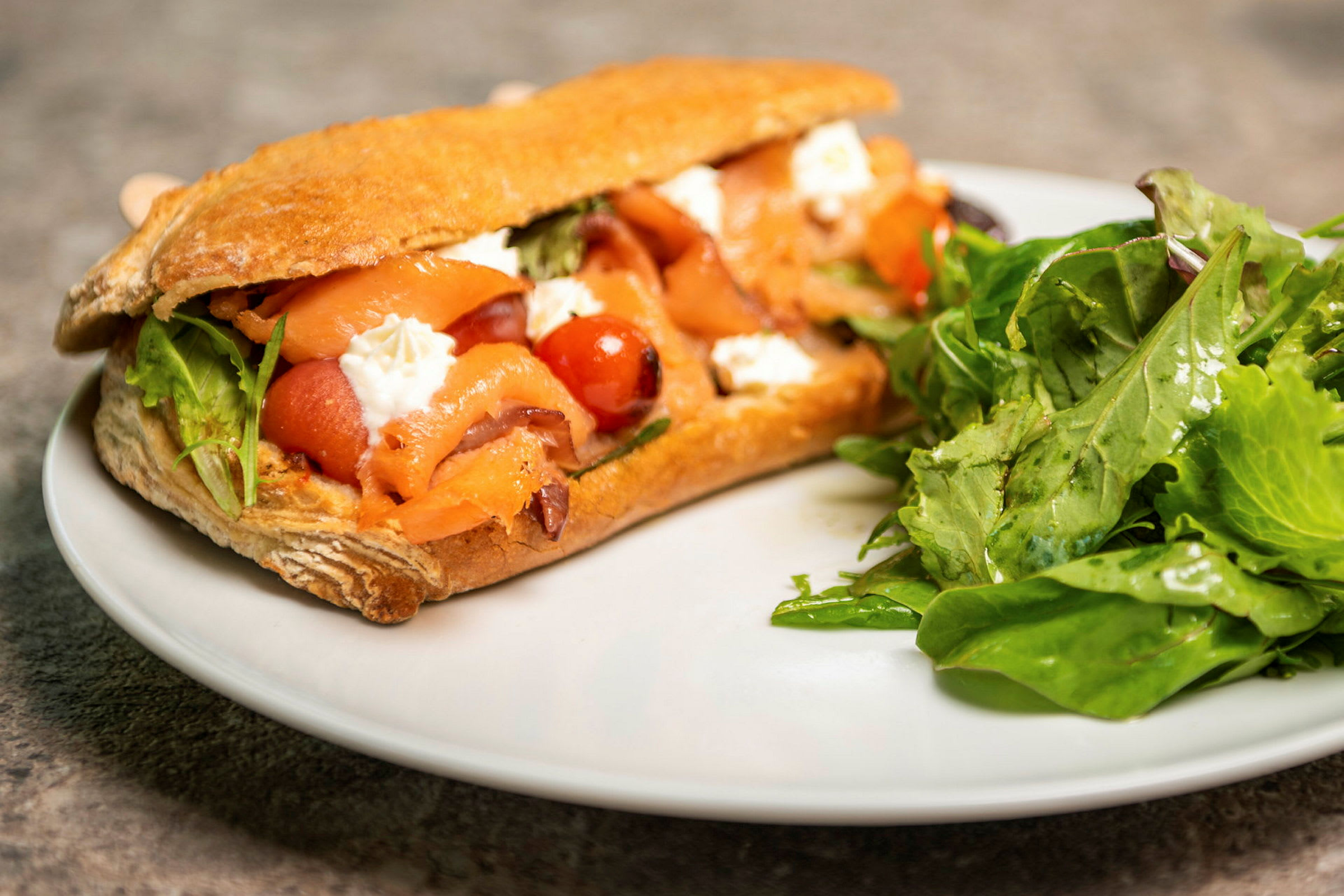 En sandwich fyldt med laks, grøntsager og ost, med en portion salat ved siden af. (AI-genereret tekst)