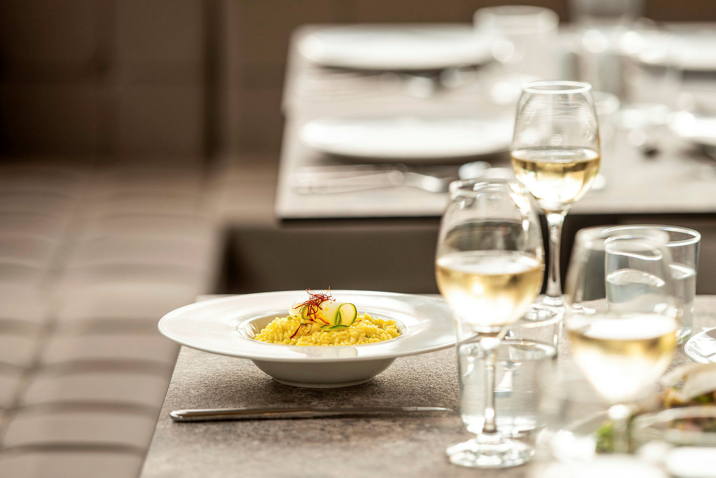 En tallerken risotto og et glas hvidvin på et dækket bord. (AI-genereret tekst)