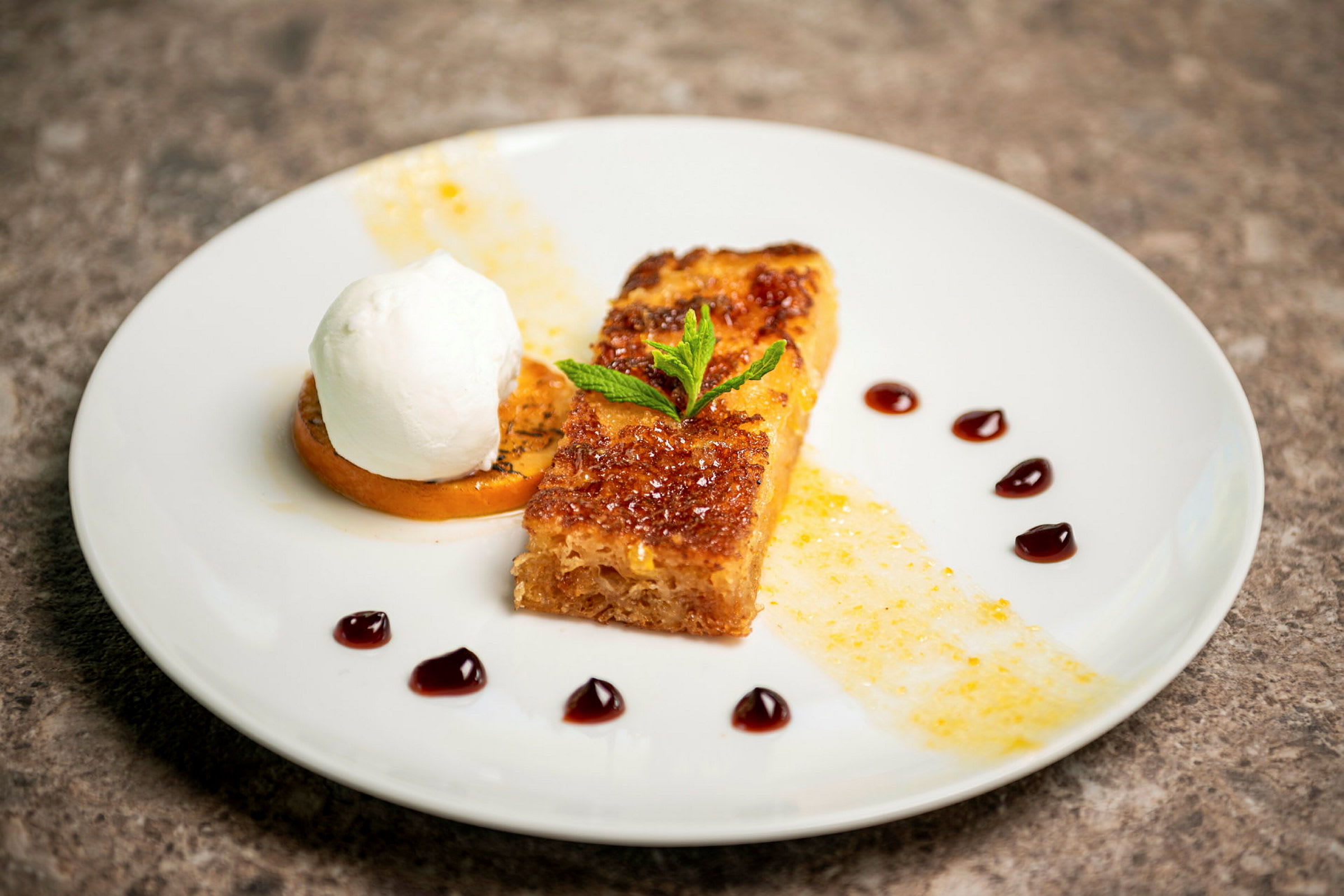 En tallerken med en dessert bestående af karamelliseret brød, fløde og garnish. (AI-genereret tekst)