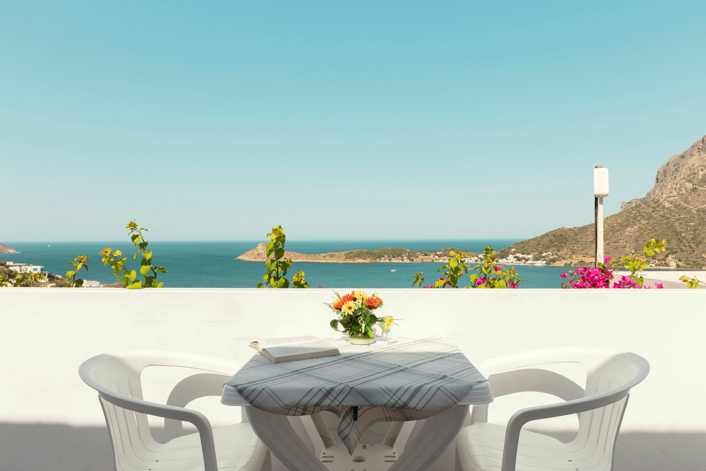 Udsigt over havet fra en balkon med et bord, to stole og en vase med blomster. (AI-genereret tekst)