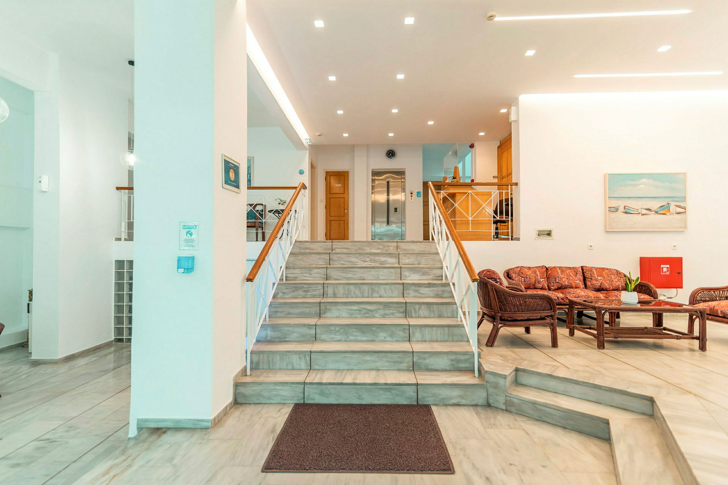 Hotellets lobby med en trappe, siddegruppe og reception. (AI-genereret tekst)