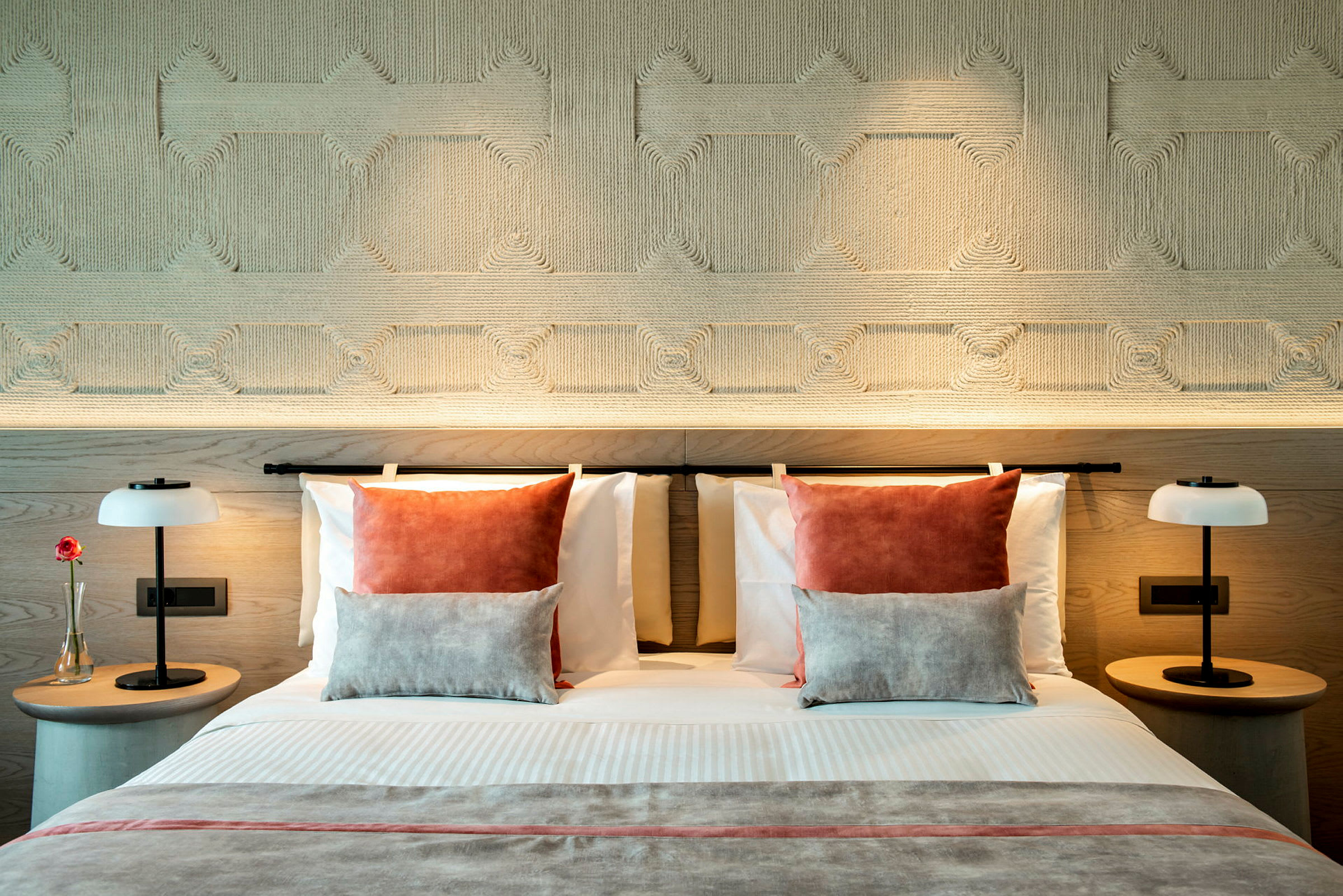 En moderne hotelseng med dekorative puder og symmetriske natborde med lamper. (AI-genereret tekst)