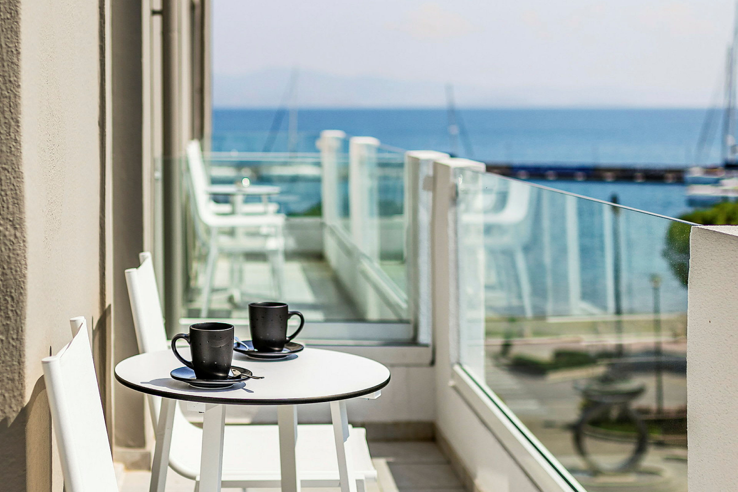 To kaffekopper på et hvidt bord på en altan med havudsigt. (AI-genereret tekst)