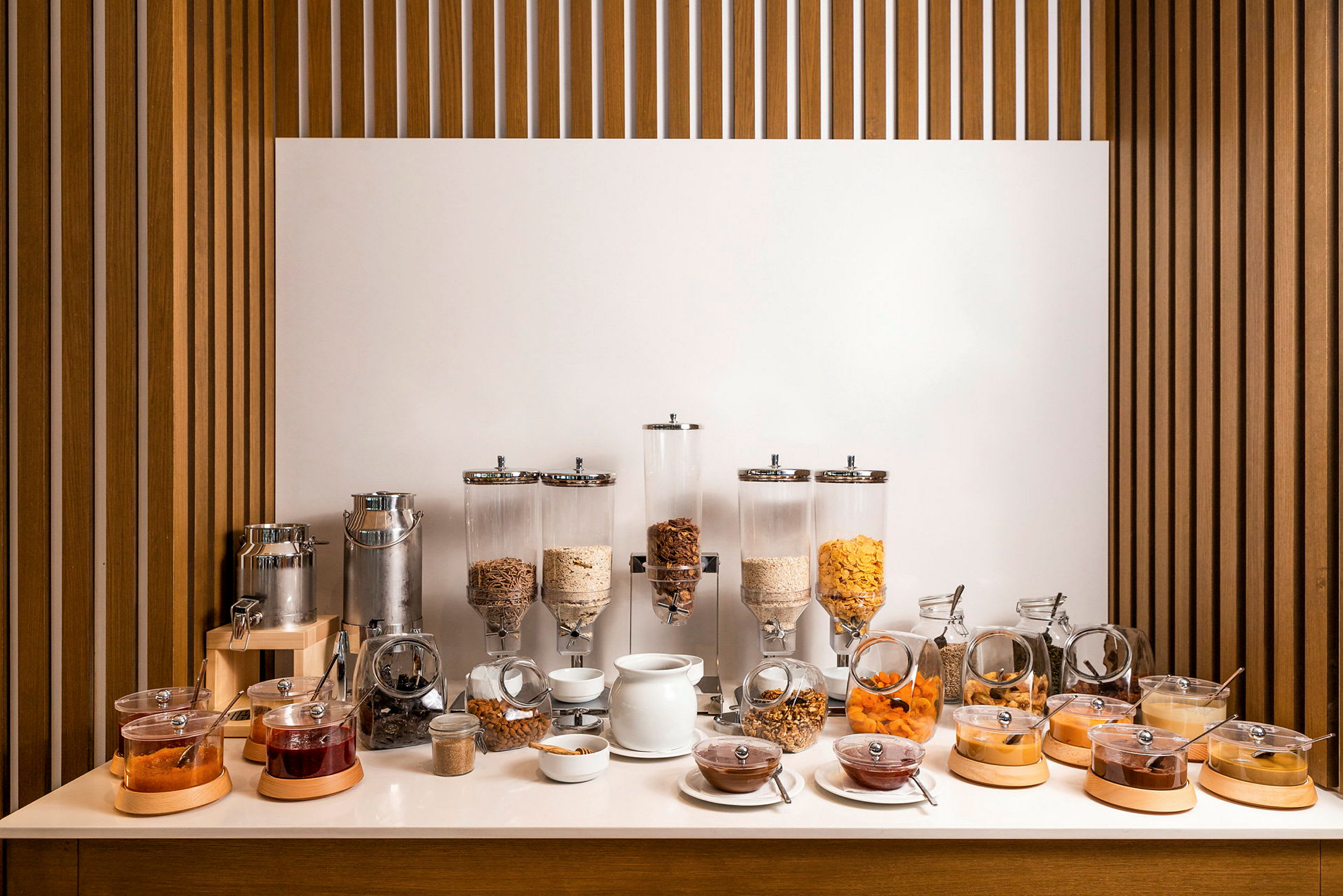 En morgenmadsbuffet med forskellige typer morgenmadsprodukter, tørret frugt, syltetøj og en væskedispenser. (AI-genereret tekst)