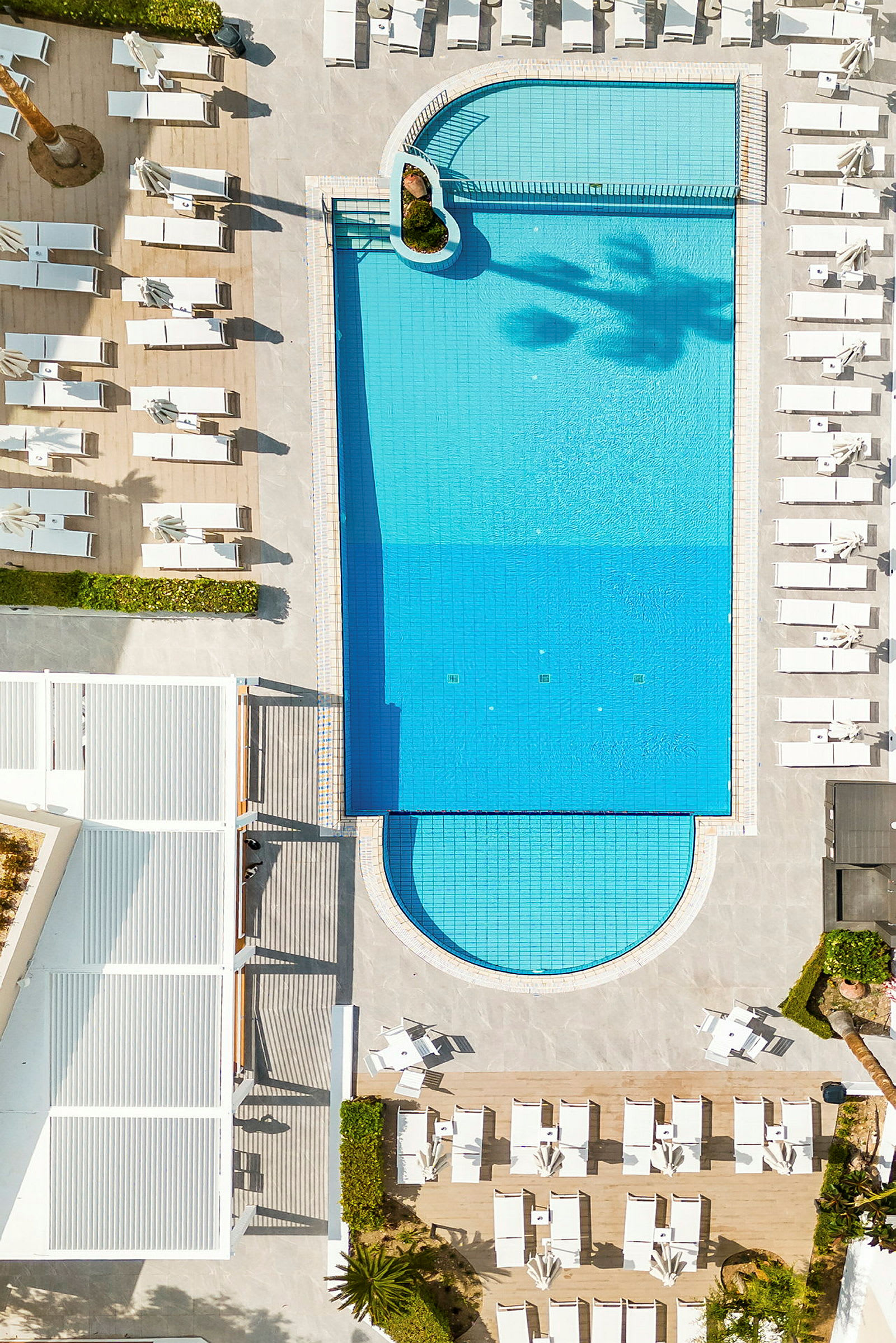 Luftfoto af en pool omgivet af liggestole og parasoller. (AI-genereret tekst)
