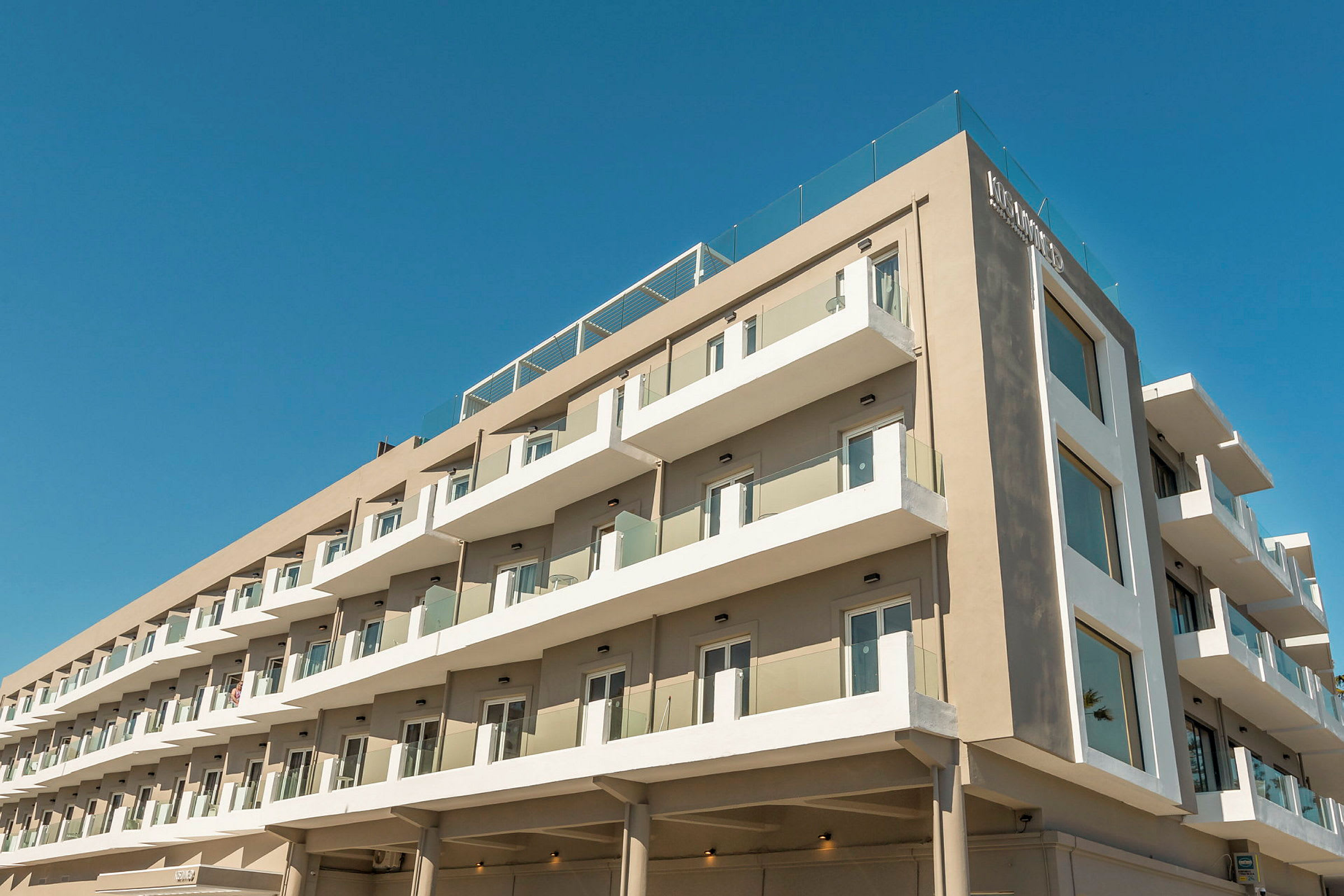 Moderne hotelbygning med flere etager og altaner under en blå himmel. (AI-genereret tekst)