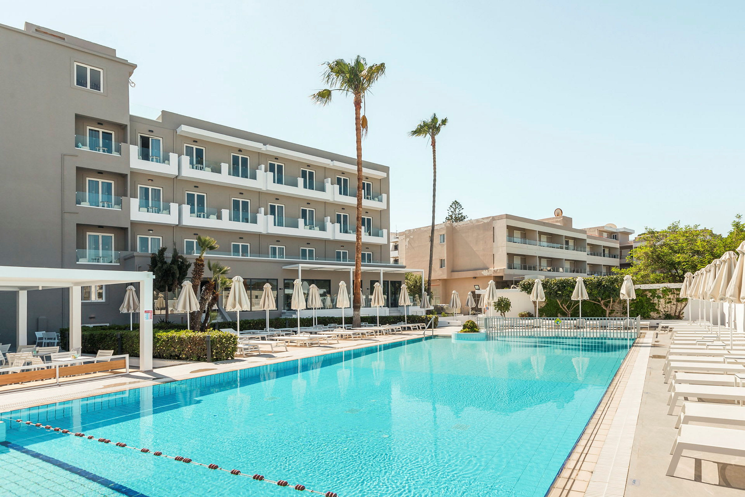 Billede af et hotel med altaner, en pool samt liggestole og parasoller. (AI-genereret tekst)