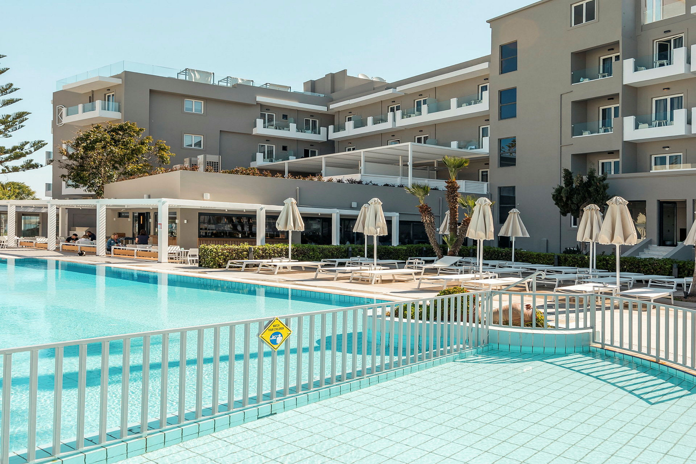 Hotelbygning med liggestole og parasoller ved poolområdet. (AI-genereret tekst)