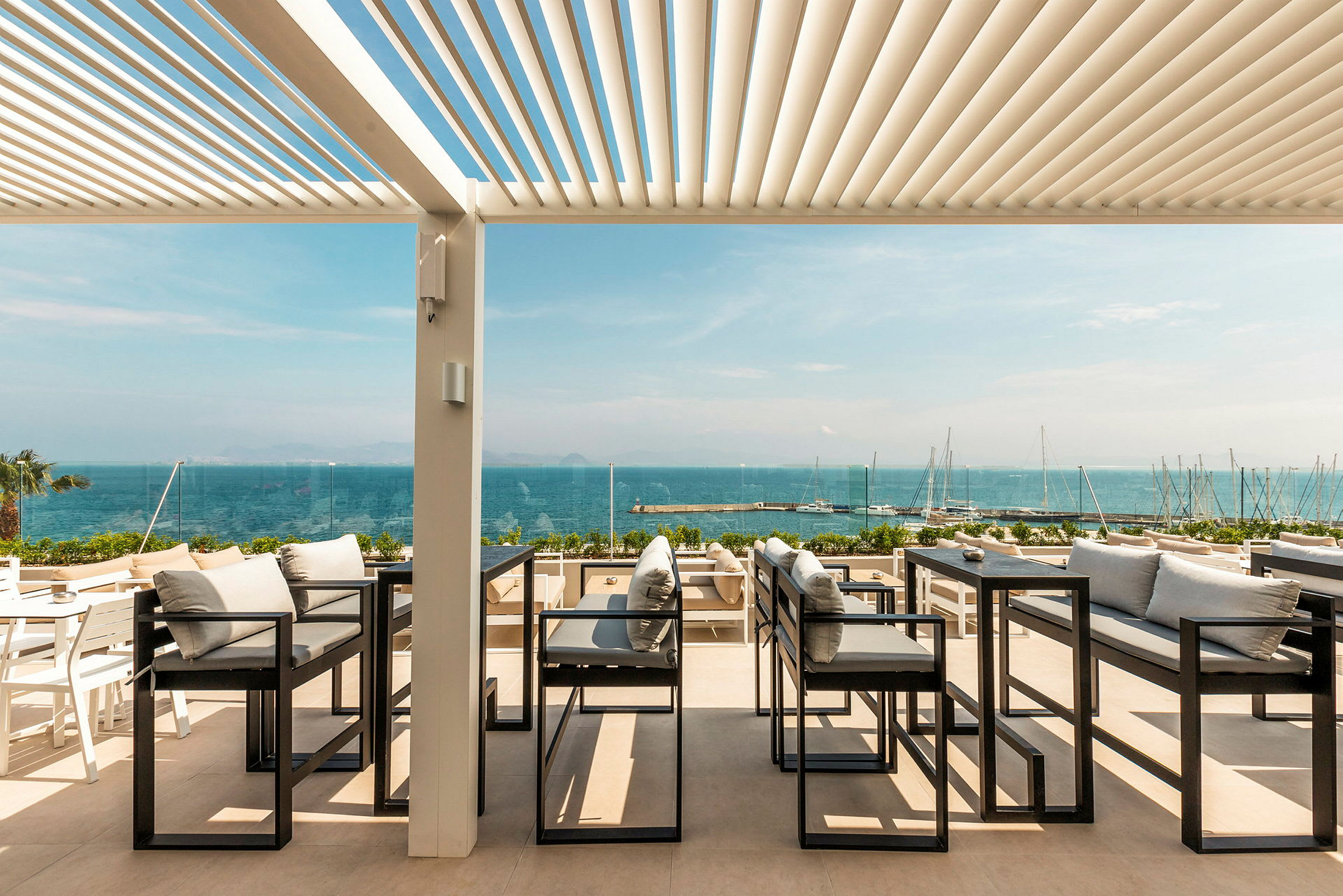 Udendørs servering med udsigt over havet, med sofaer og borde under en pergola. (AI-genereret tekst)