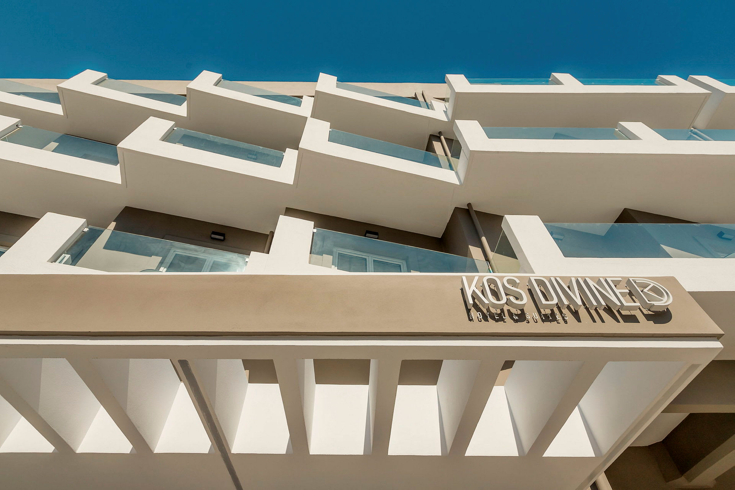 Facade af en hotelbygning med altaner i moderne stil og blå himmel i baggrunden. (AI-genereret tekst)