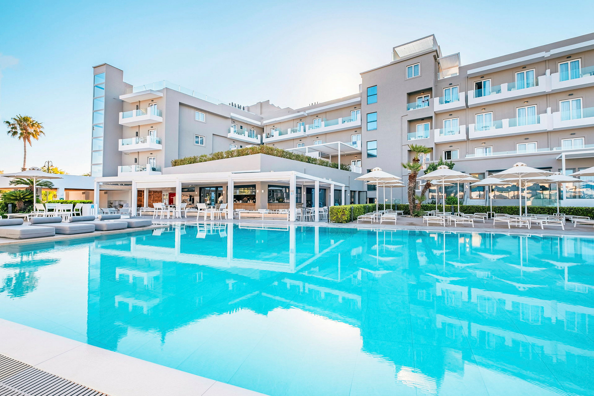 Et hotel med en stor pool foran og siddepladser under parasoller. (AI-genereret tekst)