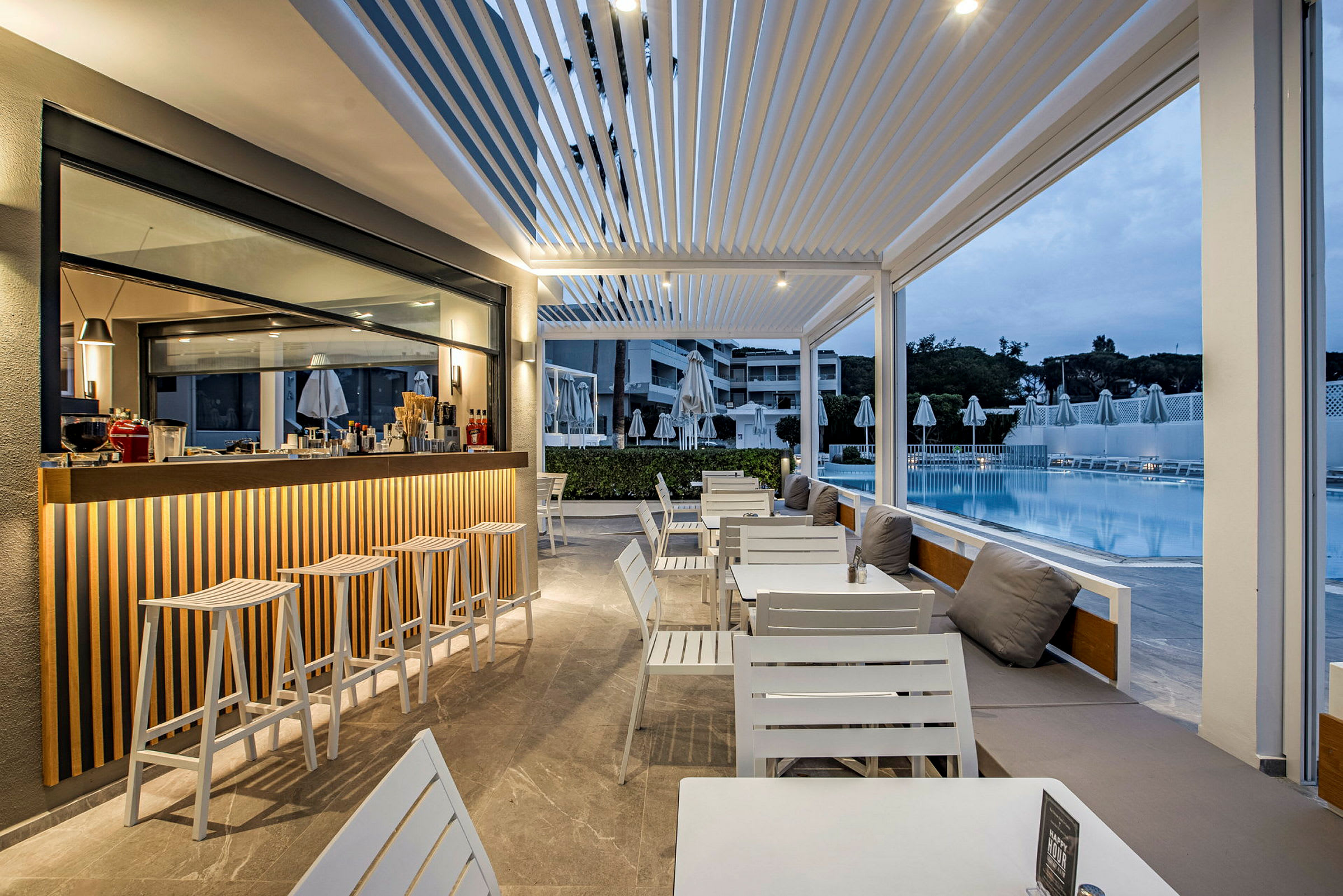 En udendørsbar og siddeområde ved en pool med moderne hvide møbler. (AI-genereret tekst)