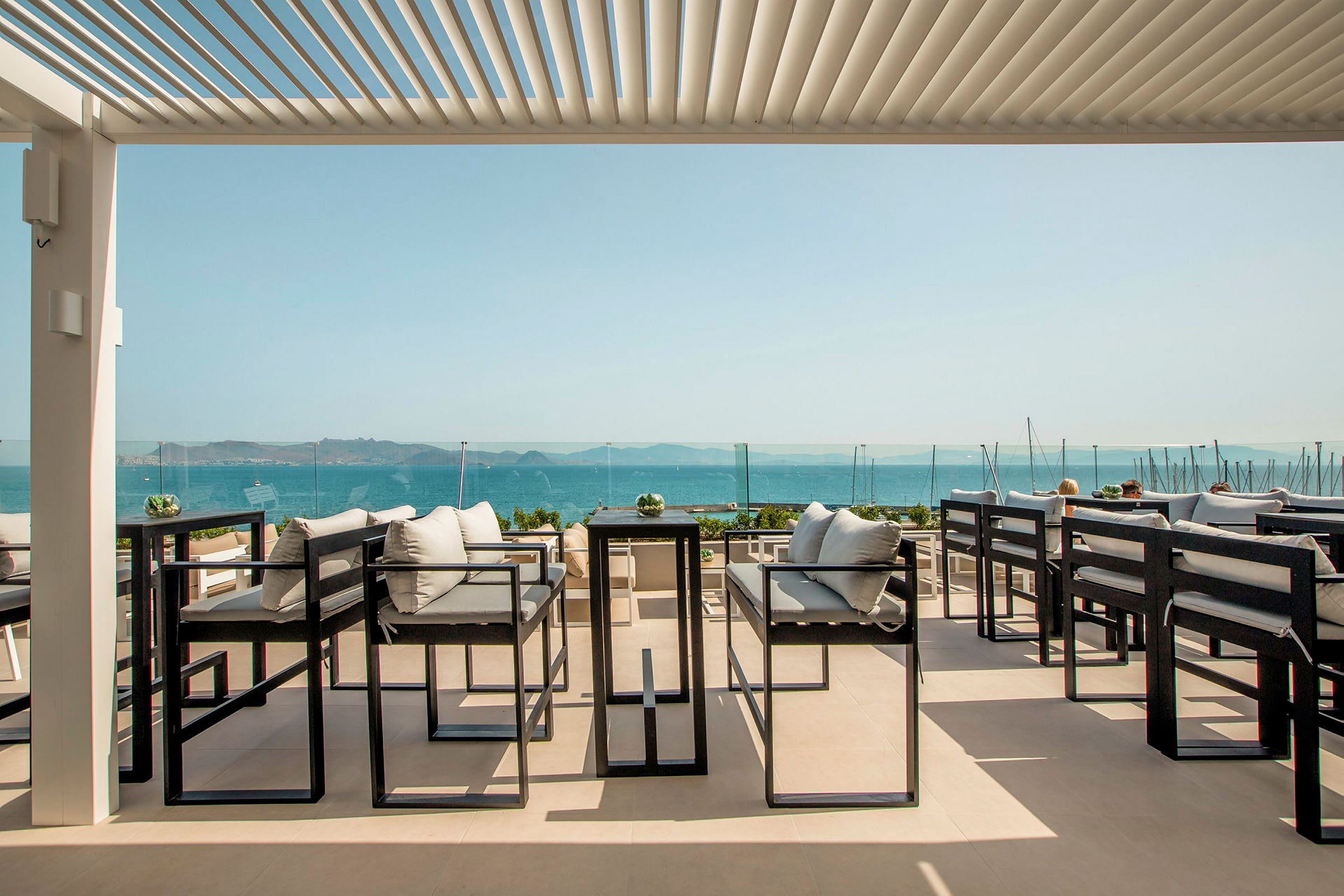 En terrasse med moderne siddepladser, udsigt over havet og en klar, blå himmel. (AI-genereret tekst)
