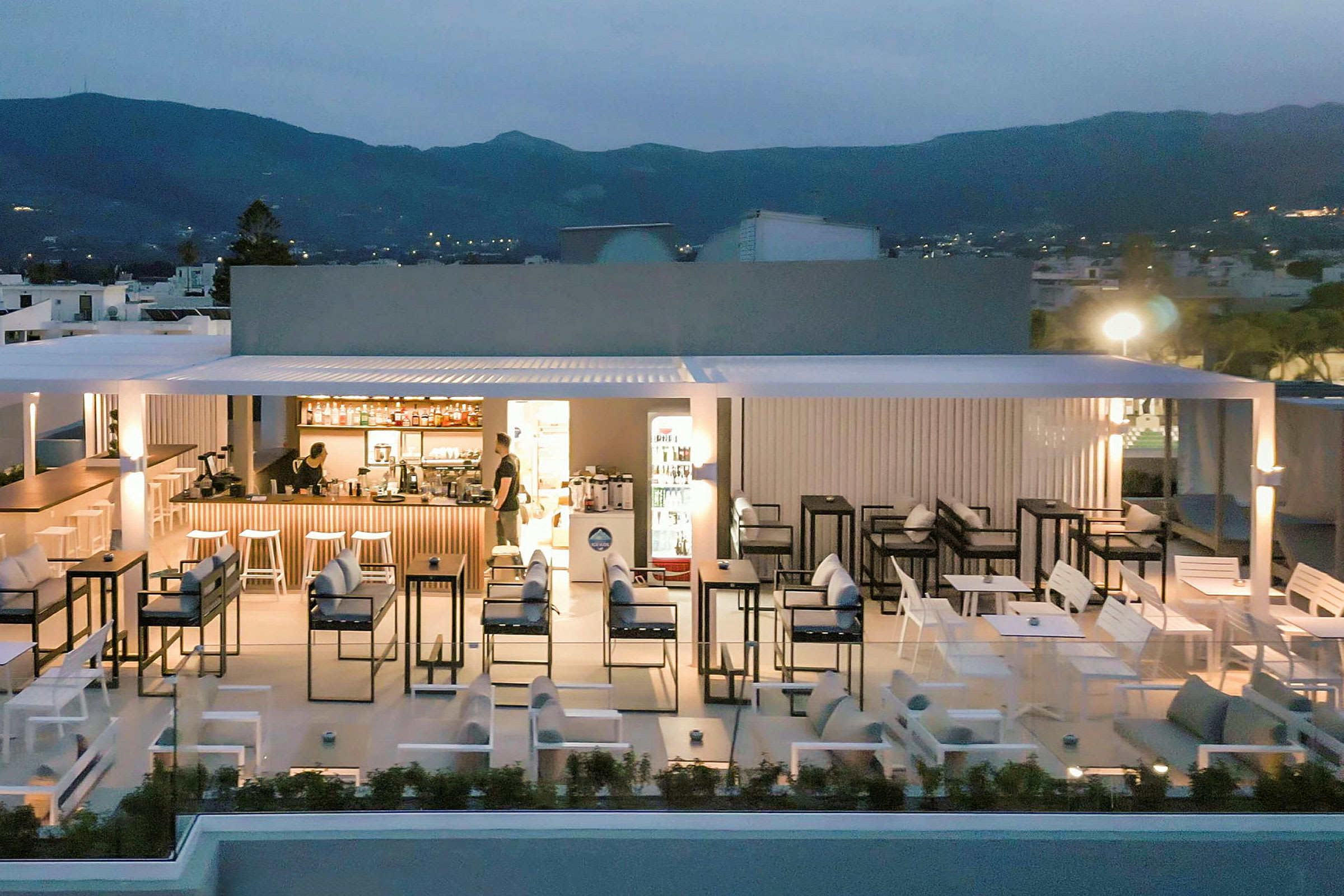 Billede af en udendørs restaurant med siddepladser og en bar på en tagterrasse i skumringen. (AI-genereret tekst)
