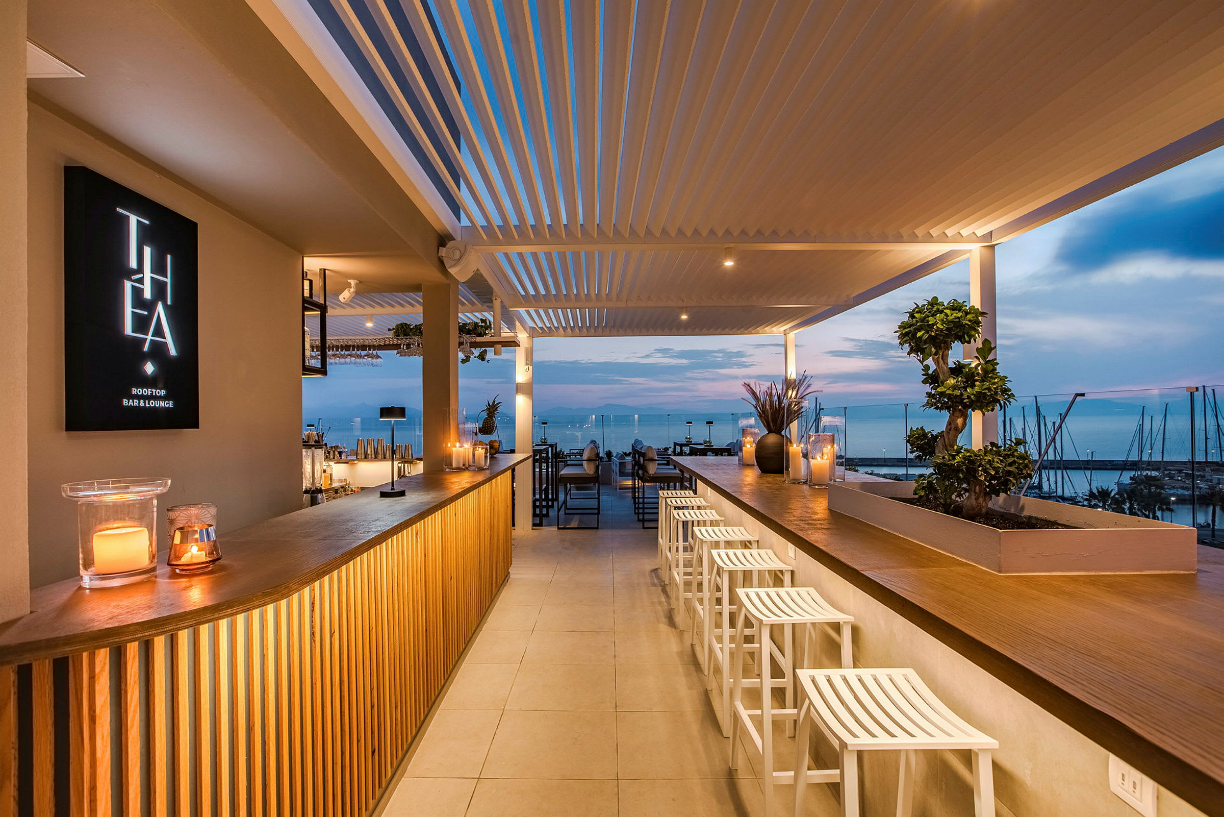 En moderne tagterrassebar med udsigt over havet i solnedgangen. Baren er oplyst og hyggeligt indrettet. (AI-genereret tekst)
