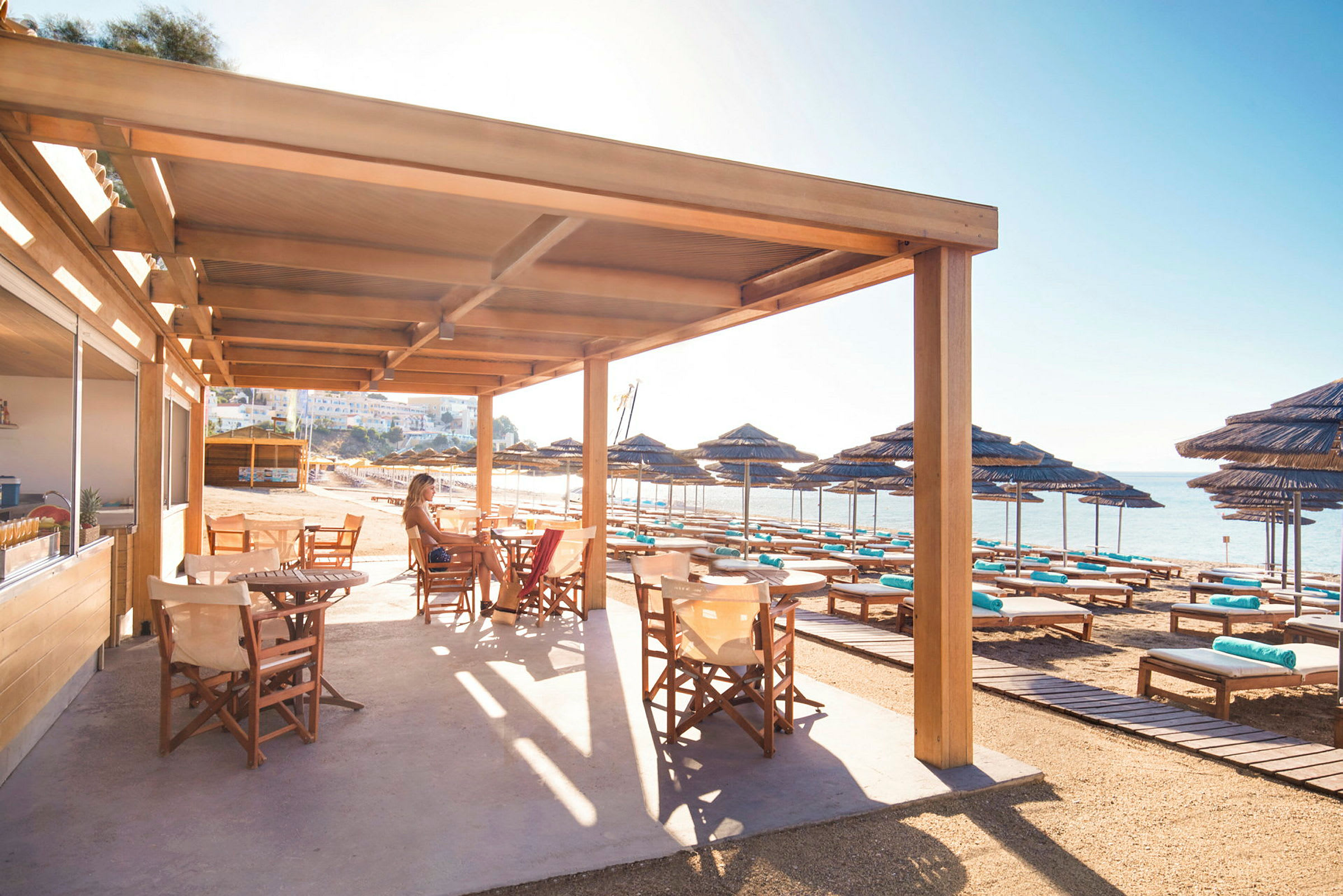 Terrasse med træstole under solafskærmning ved en strand. (AI-genereret tekst)