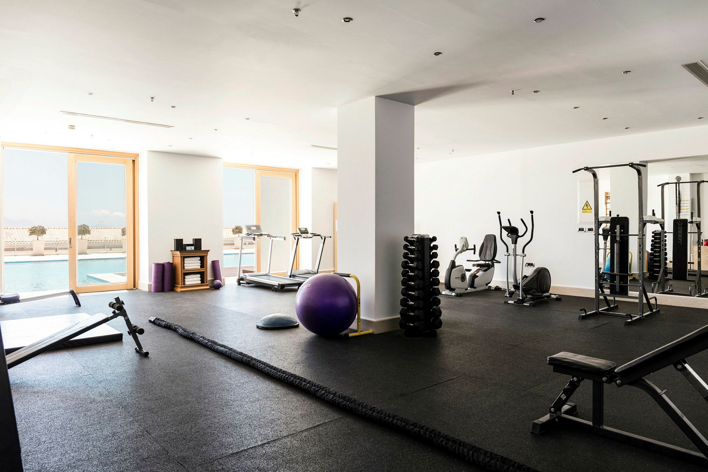 Billede af et fitnesscenter med træningsudstyr og udsigt mod en pool. (AI-genereret tekst)