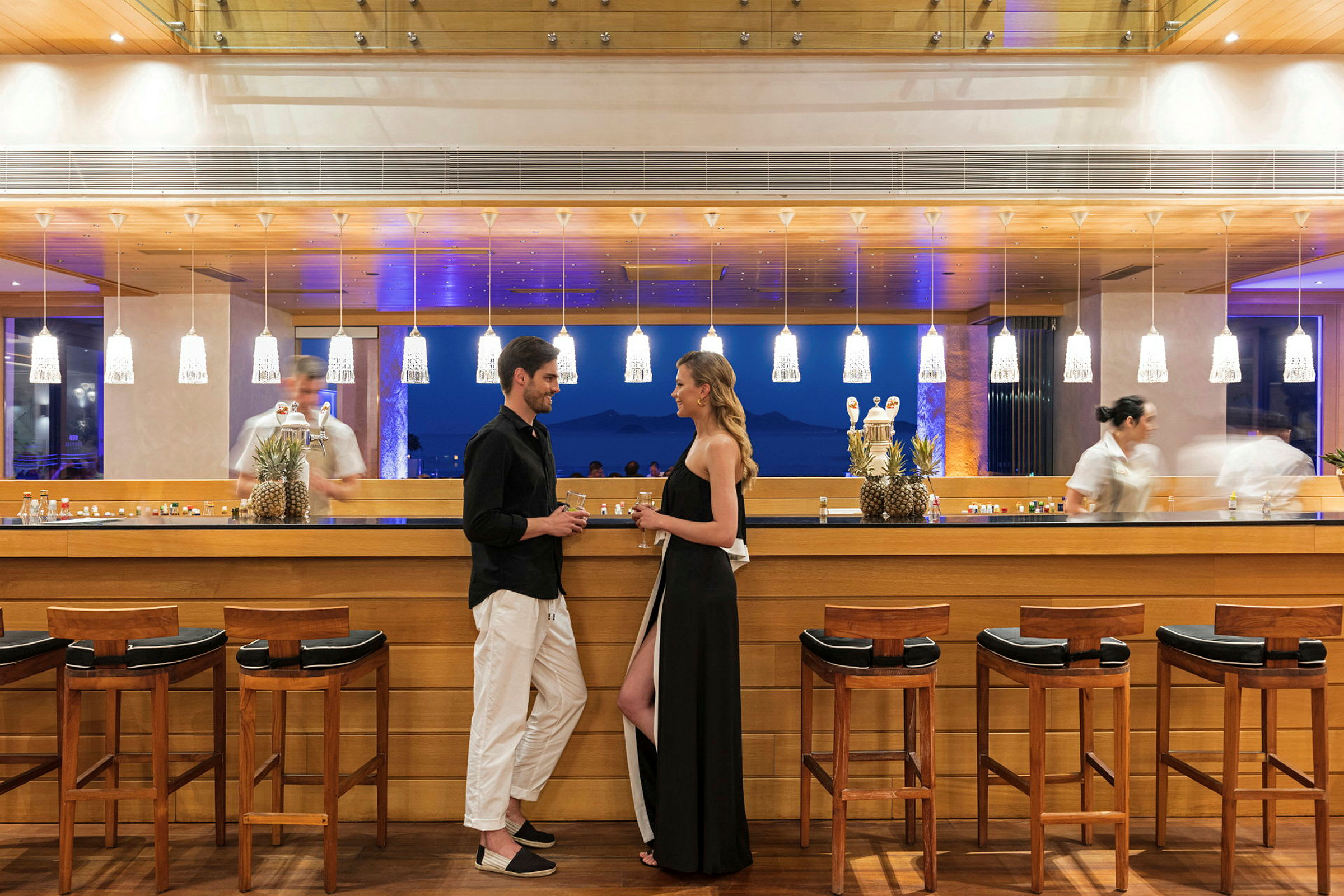 Personer står ved en elegant bar med træinteriør og belysning. (AI-genereret tekst)