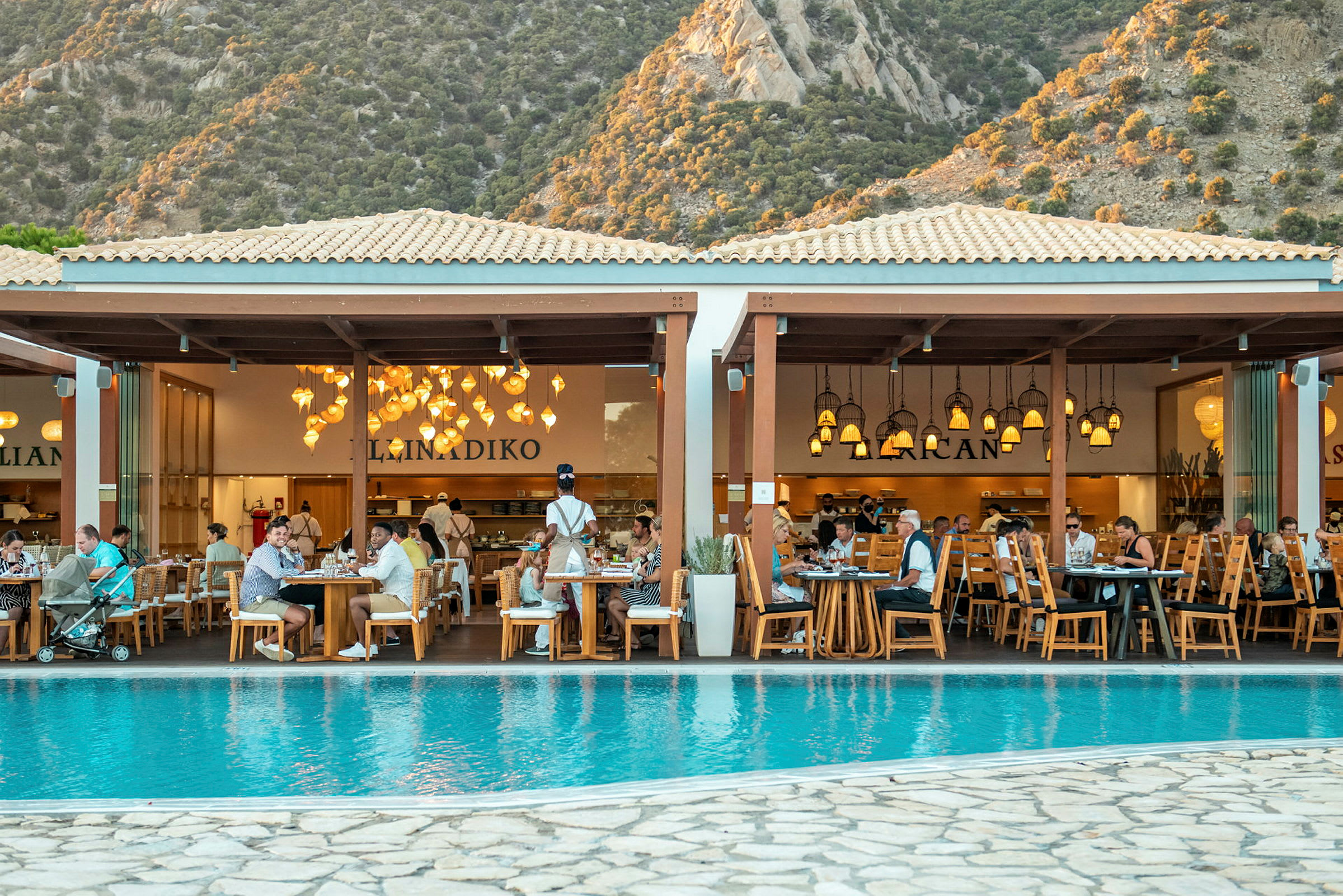 En restaurant ved en pool med bjerge i baggrunden. (AI-genereret tekst)