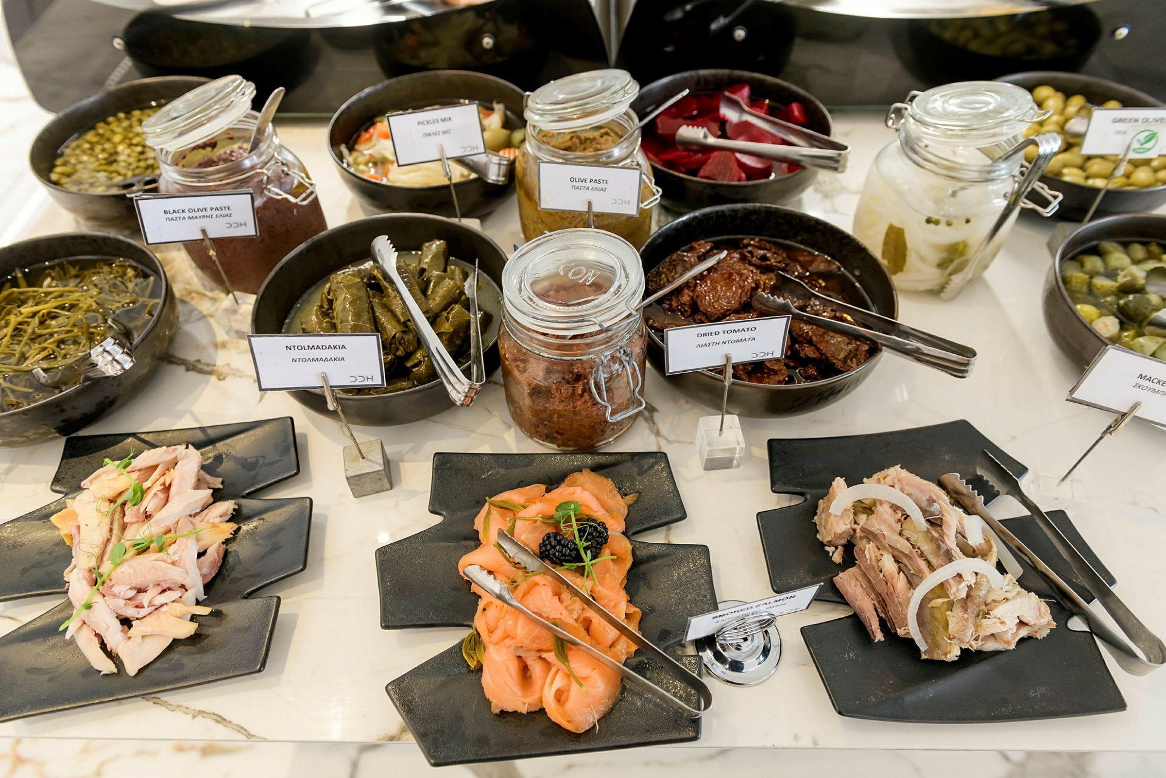Buffet med forskellige typer forretter og småretter, inklusive syltede madvarer og pålæg på tallerkener. (AI-genereret tekst)