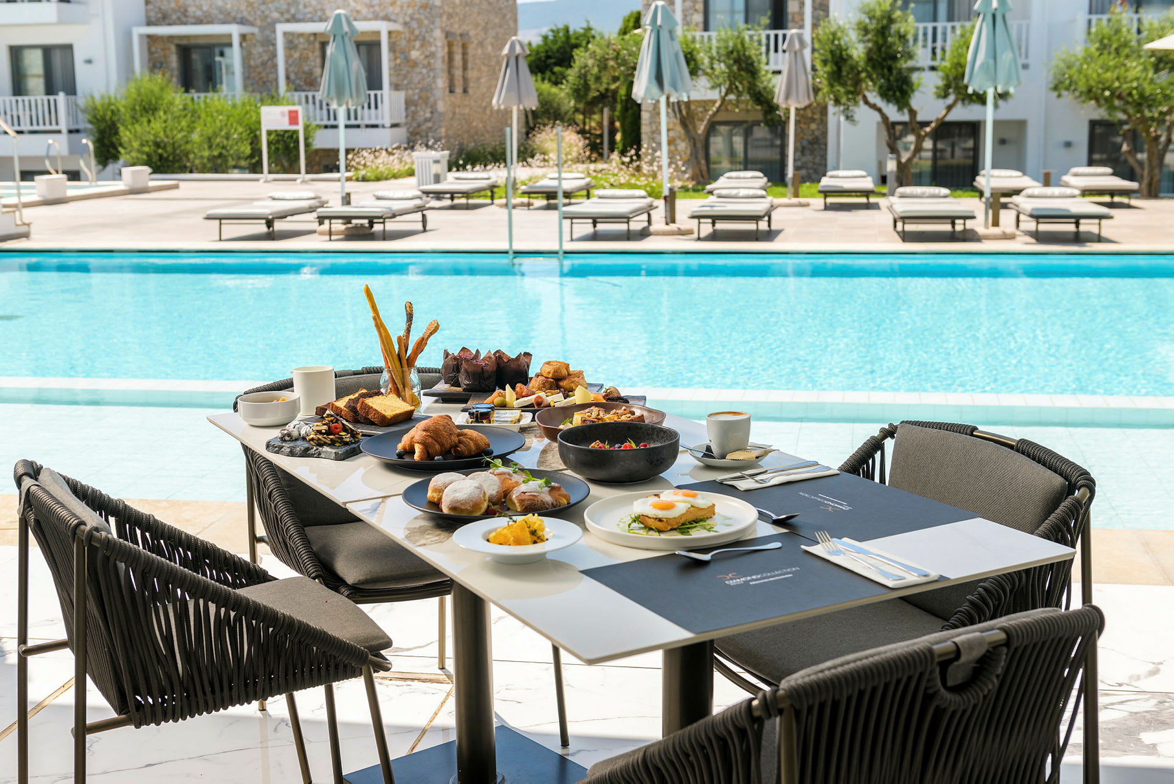 Morgenbord ved en pool med en ferieresort i baggrunden. (AI-genereret tekst)