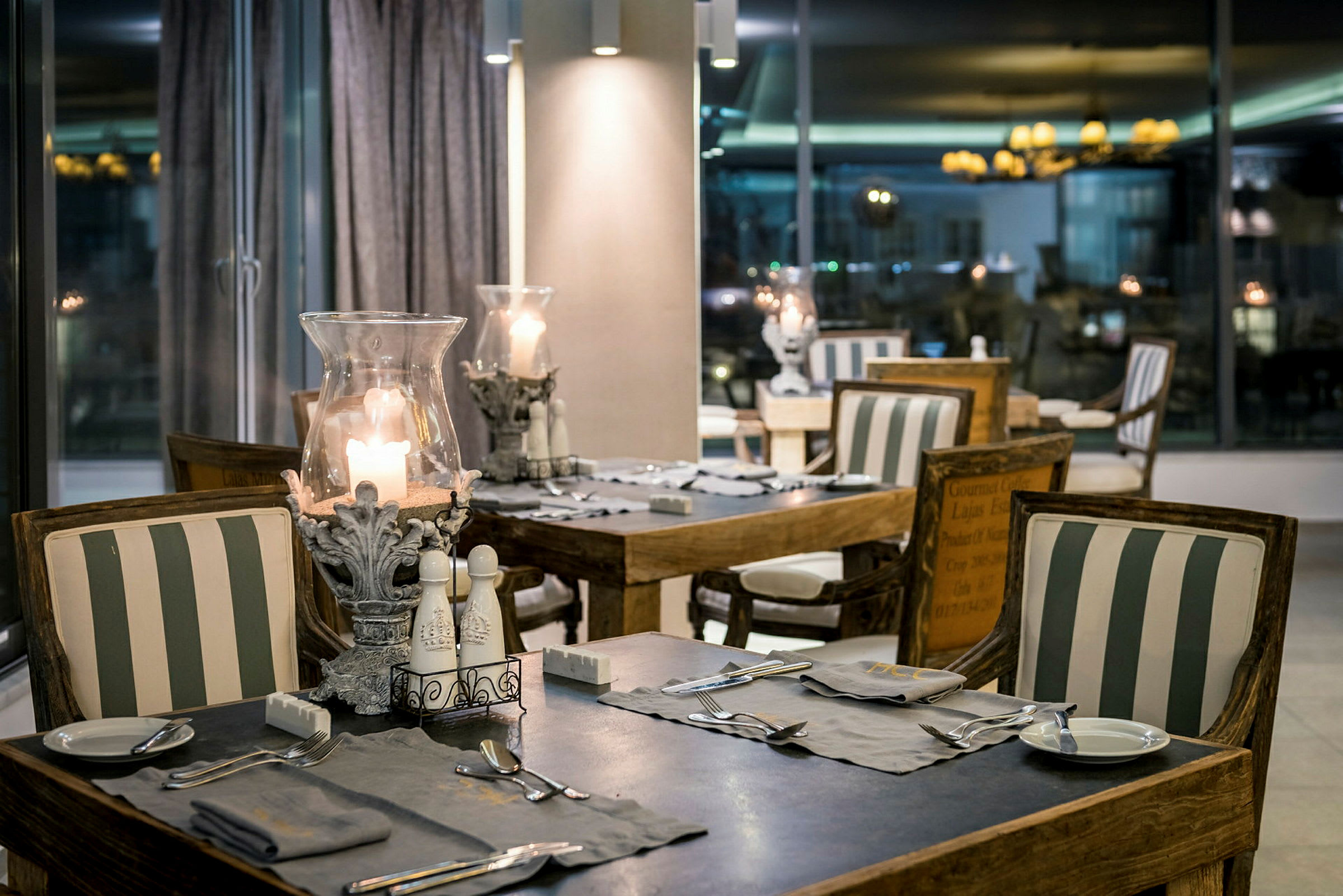 En restaurant med borde og stole dekoreret med stribede puder og tændte lys. (AI-genereret tekst)