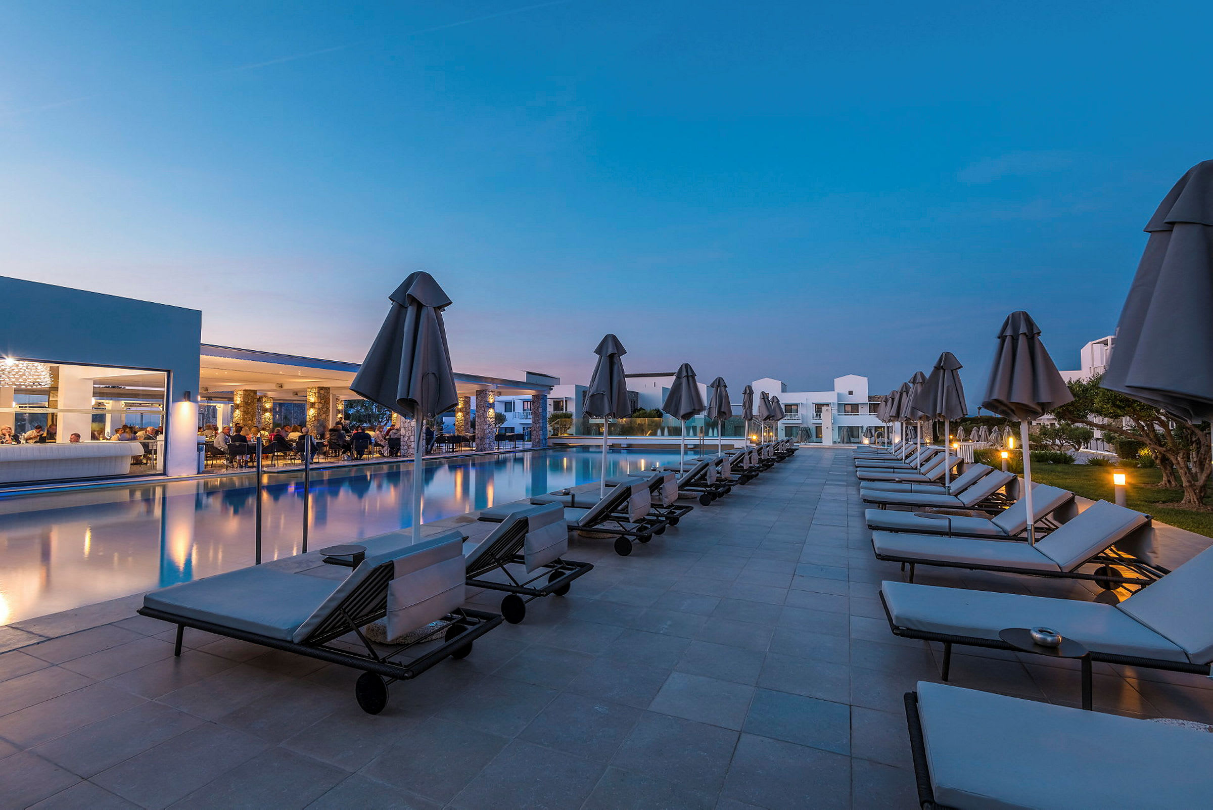 En hotelpool med liggestole og parasoller ved skumringen. (AI-genereret tekst)