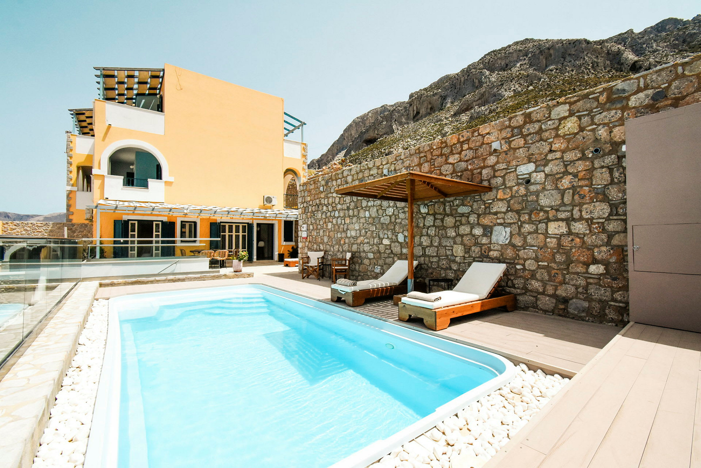 En swimmingpool foran et gult hus og en stenmur. (AI-genereret tekst)