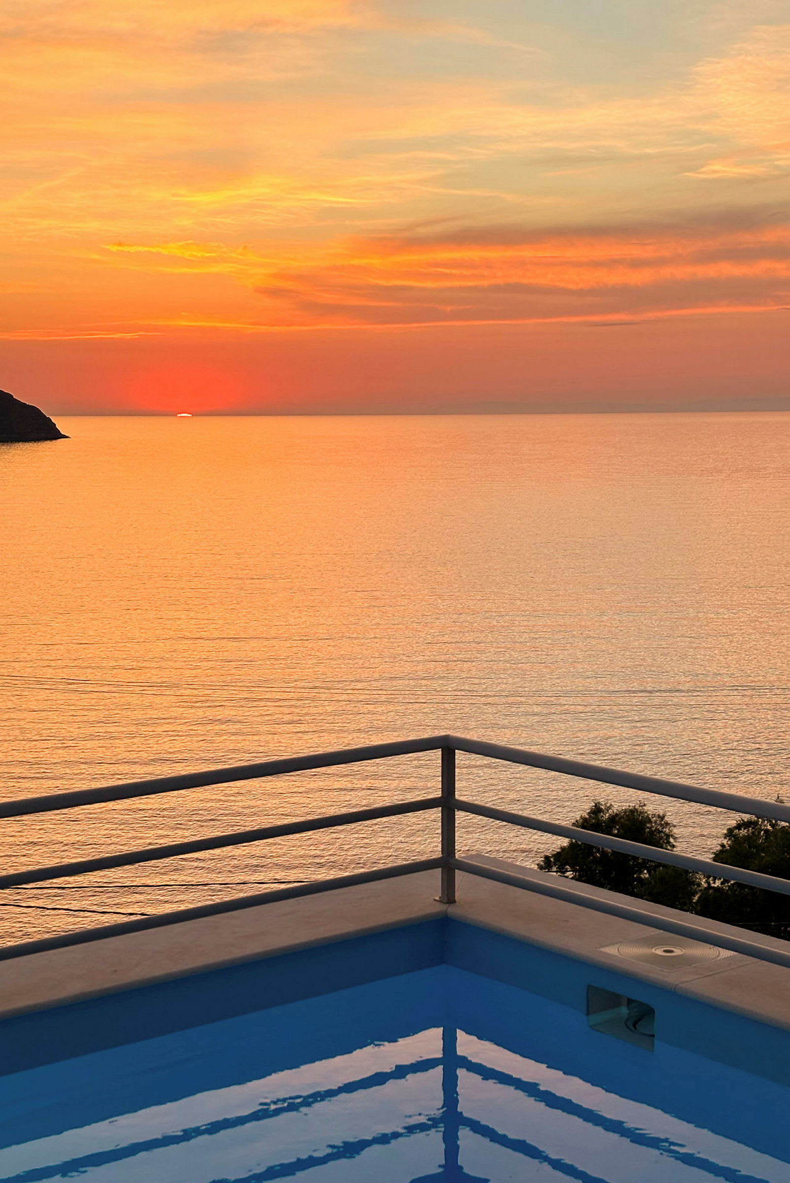 Solnedgang over havet med en pool omkranset af et rækværk i forgrunden. (AI-genereret tekst)