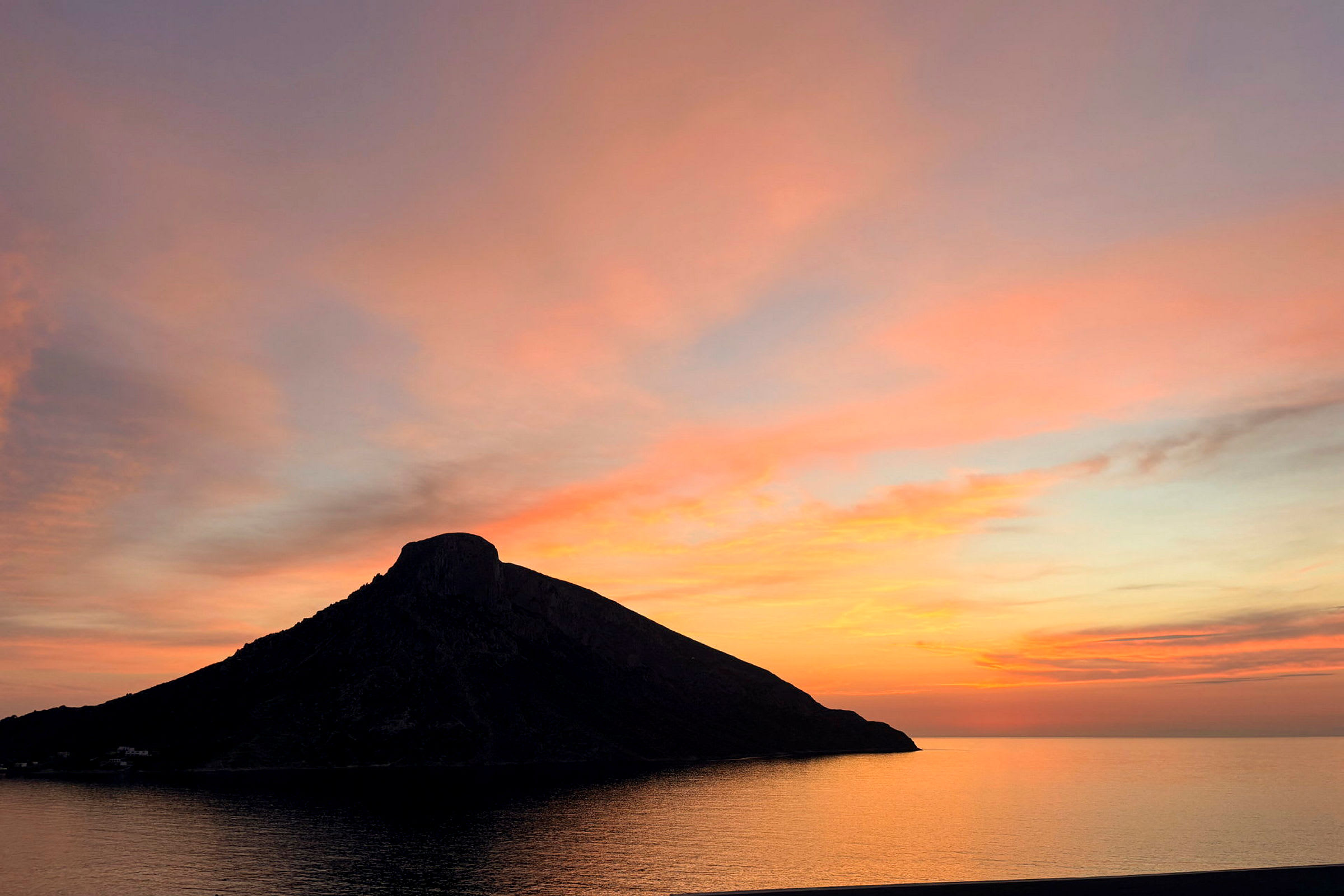 En silhuet af en bakke ved havet mod en farverig solnedgang. (AI-genereret tekst)