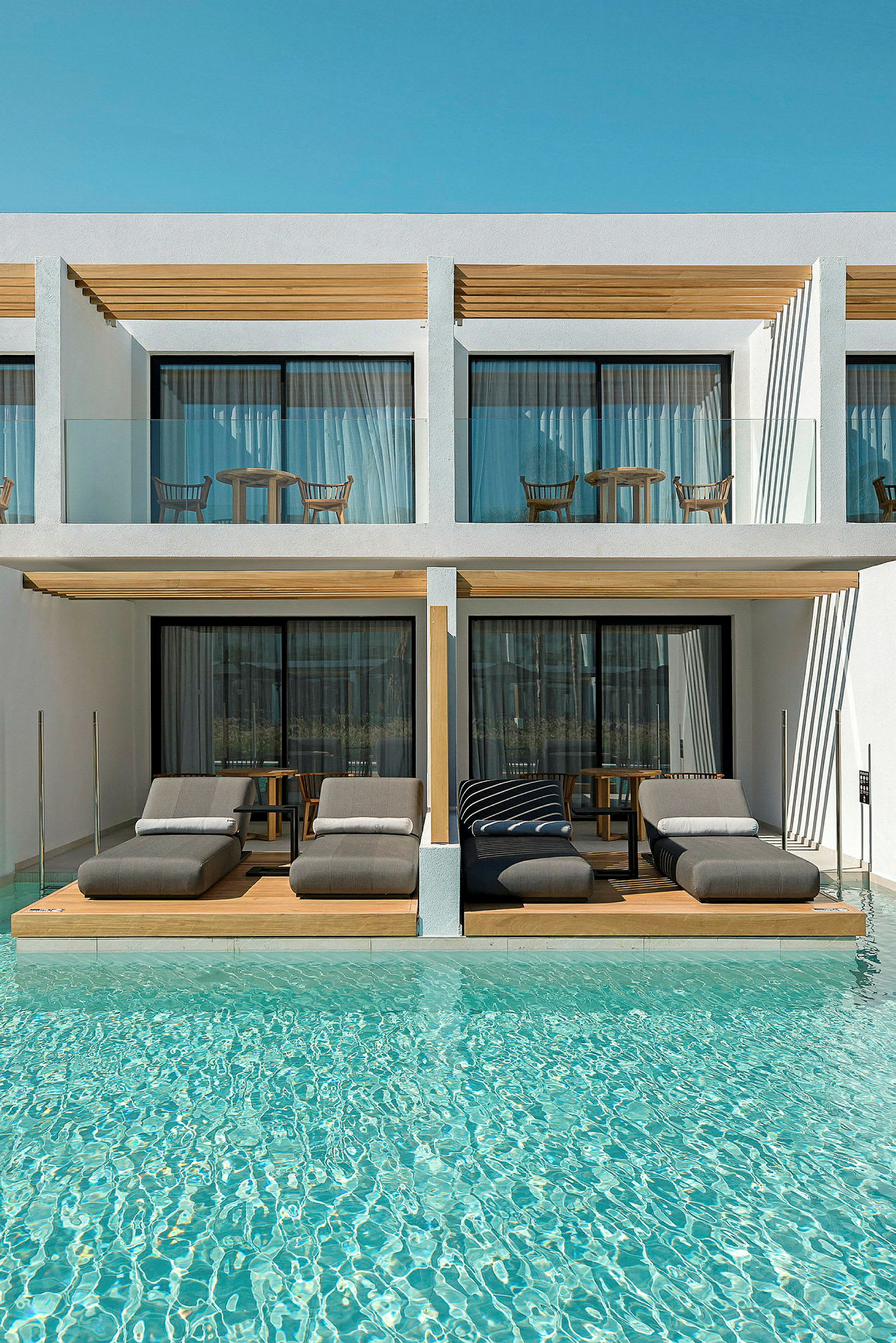 Luksuriøse liggestole ved en pool foran moderne hotelværelser. (AI-genereret tekst)