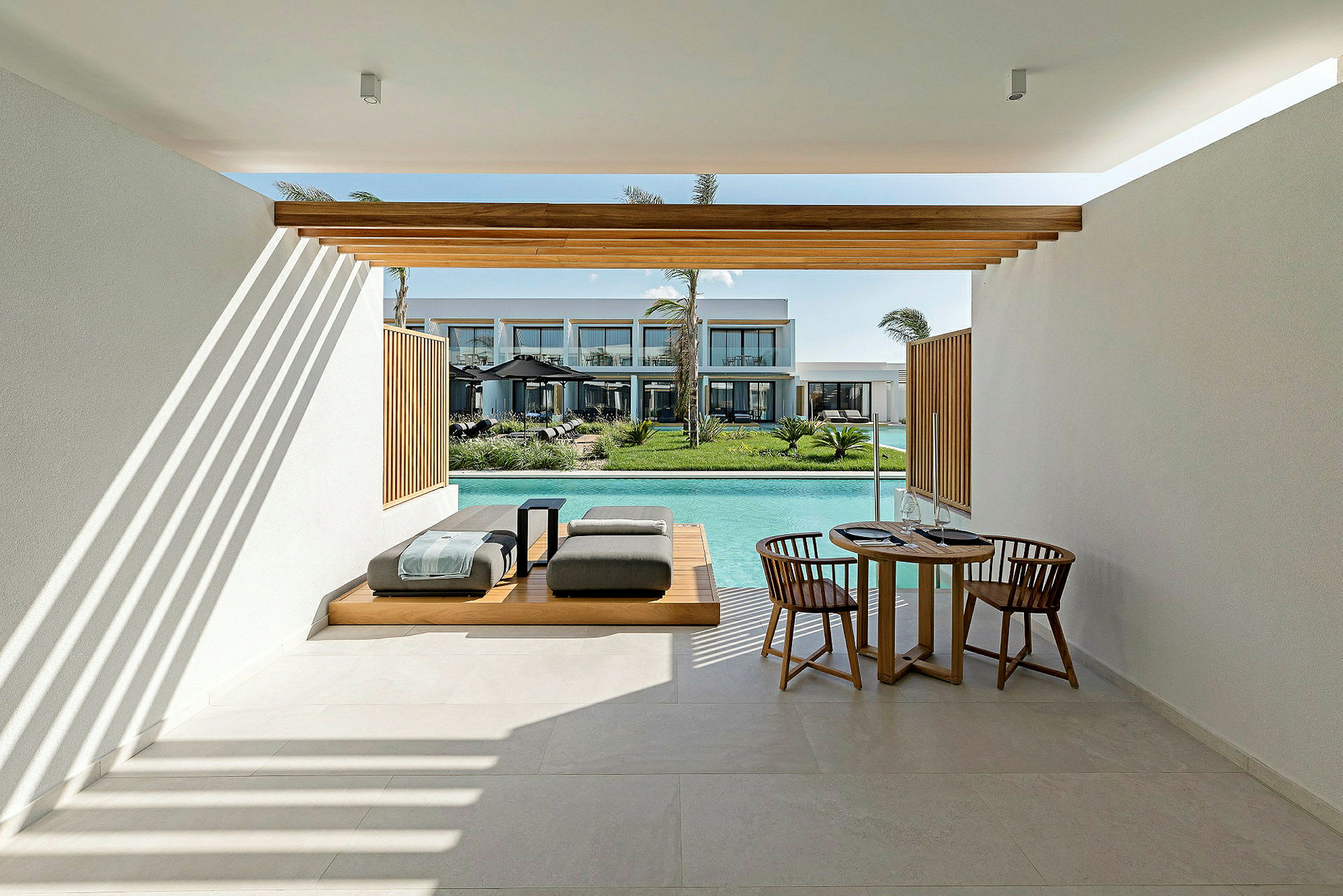 Udendørsområde med siddepladser og spisebord, med udsigt til pool og bygninger i baggrunden. (AI-genereret tekst)