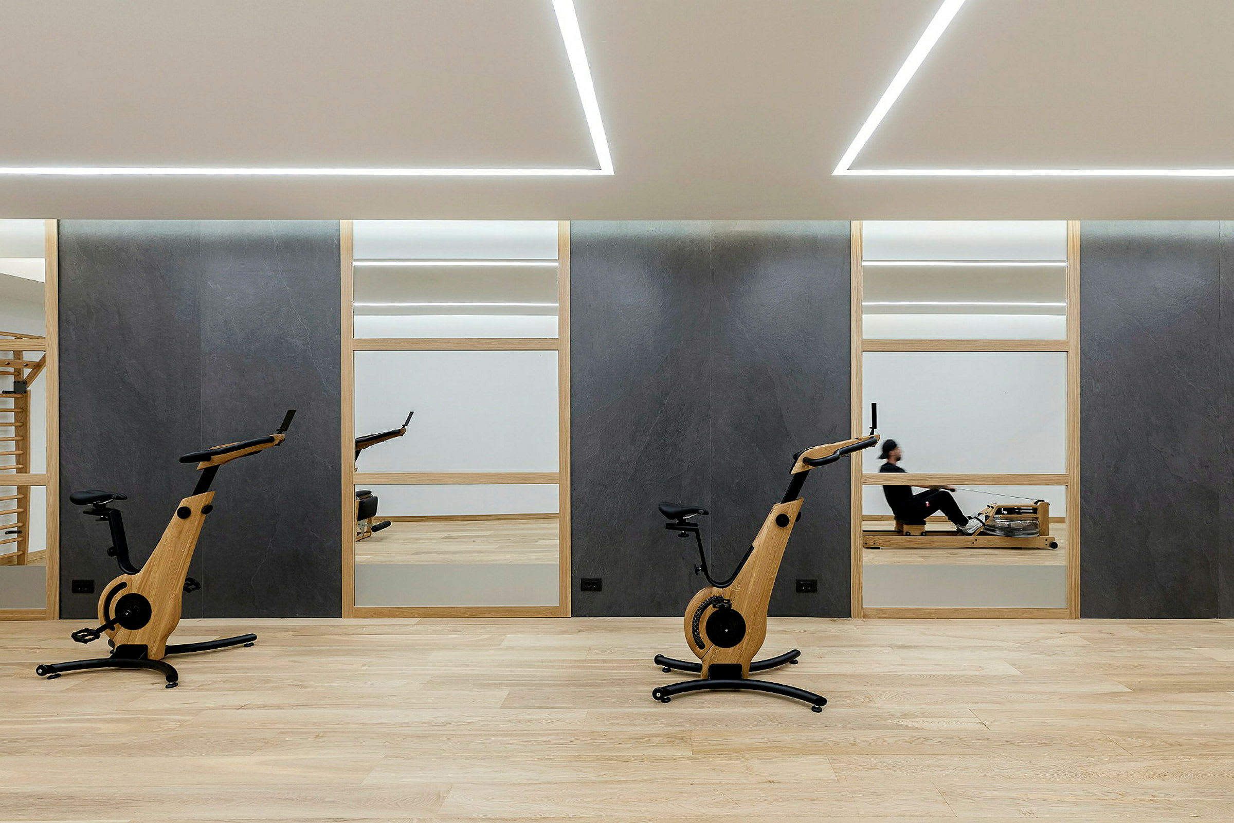 Fitnesscenter med to motionscykler og en person på en romaskine. (AI-genereret tekst)