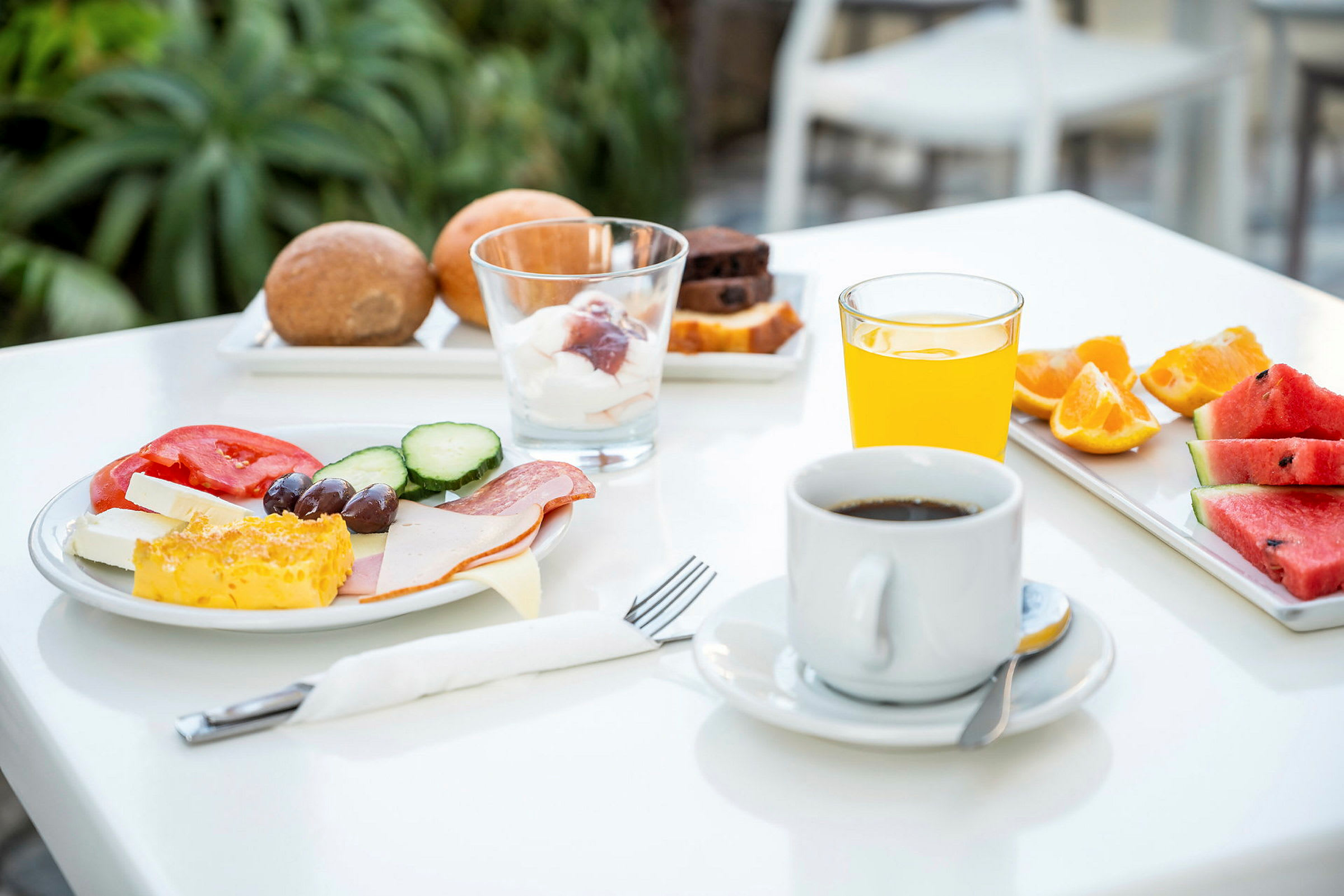 En morgenmad med kaffe, appelsinjuice, brød, frugt og grøntsager på et bord. (AI-genereret tekst)