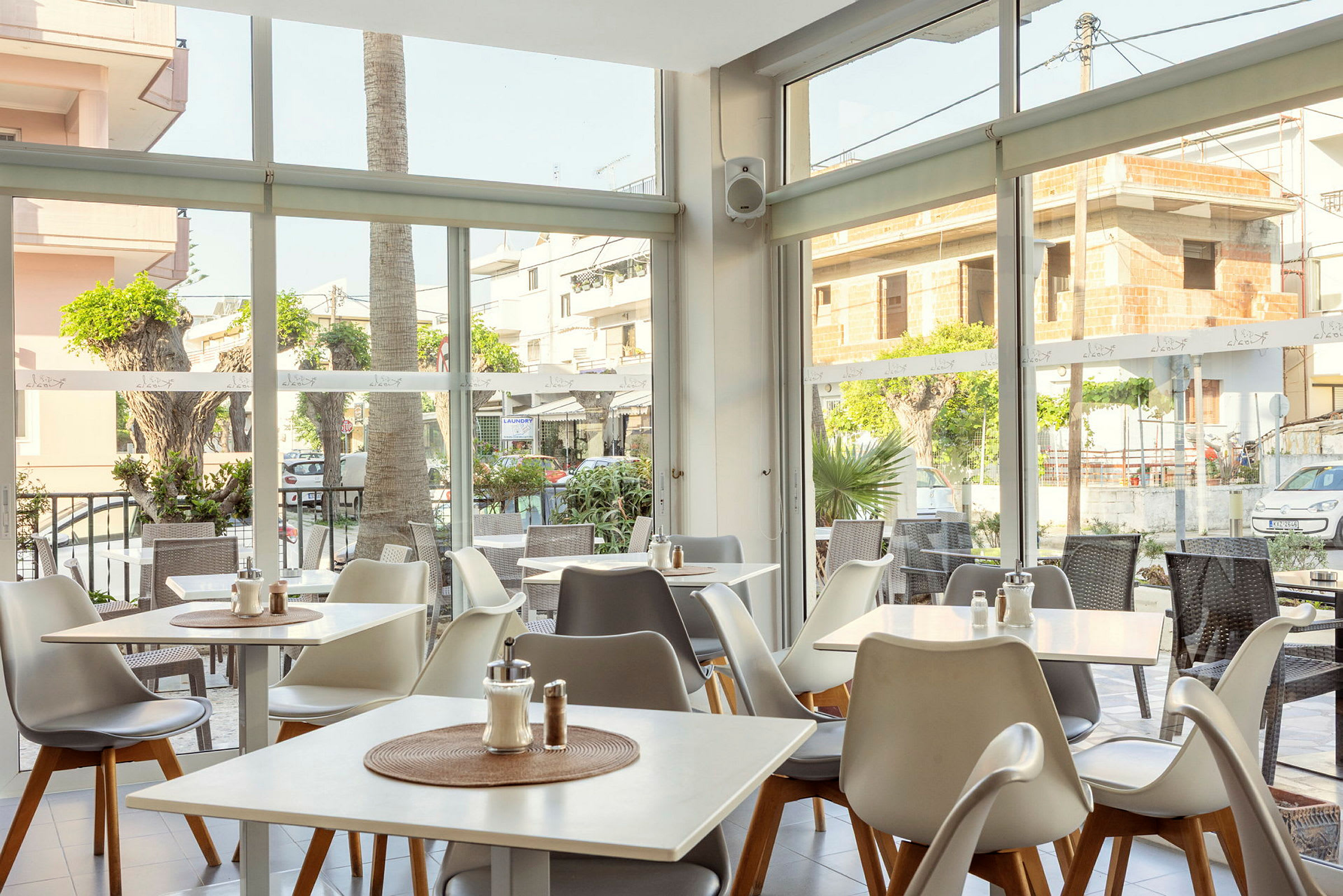 En lys restaurant med vinduer ud mod gaden og udendørs borde. (AI-genereret tekst)