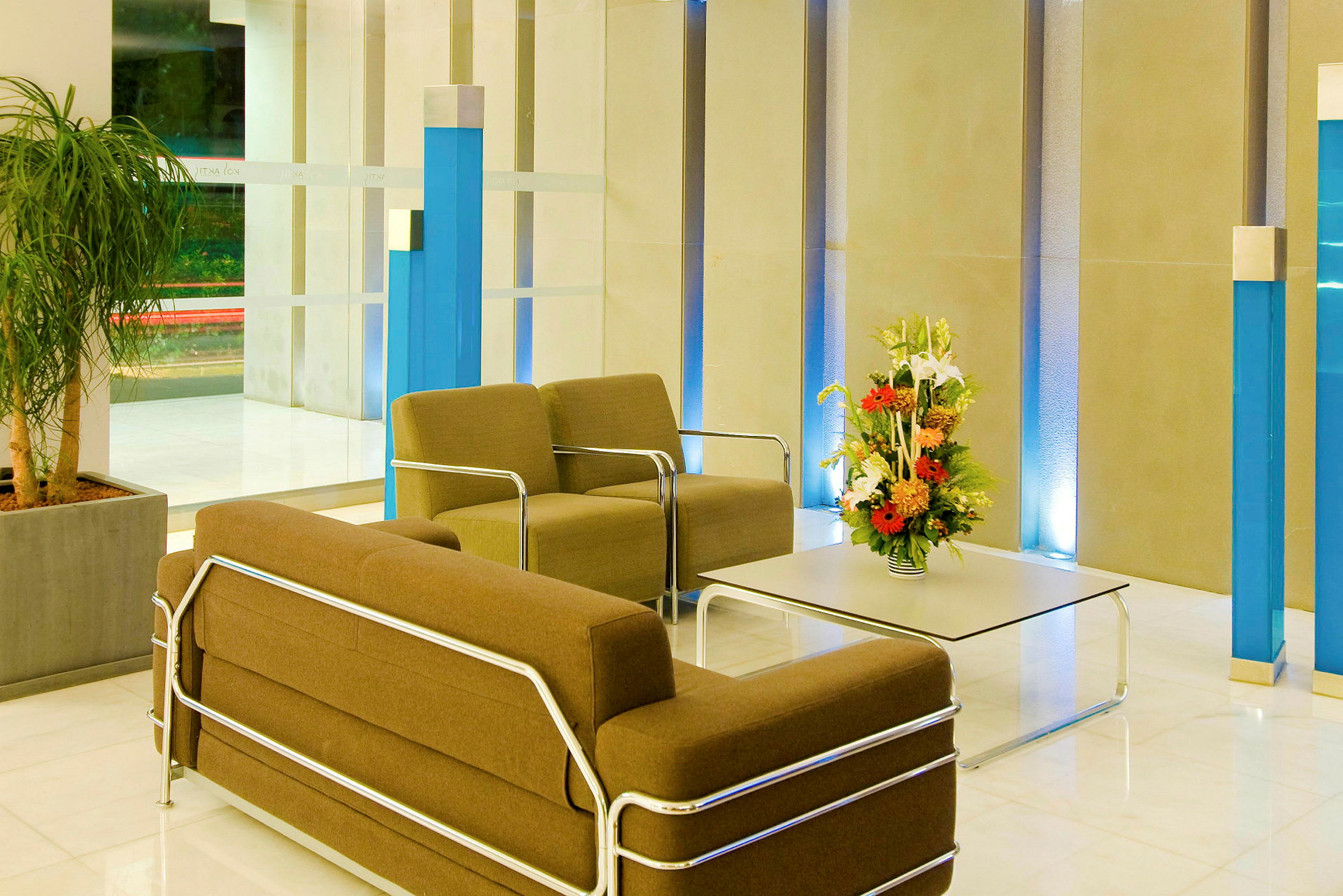 Billede af en hotellobby med stole og bord, udsmykket med en blomsterdekoration. (AI-genereret tekst)