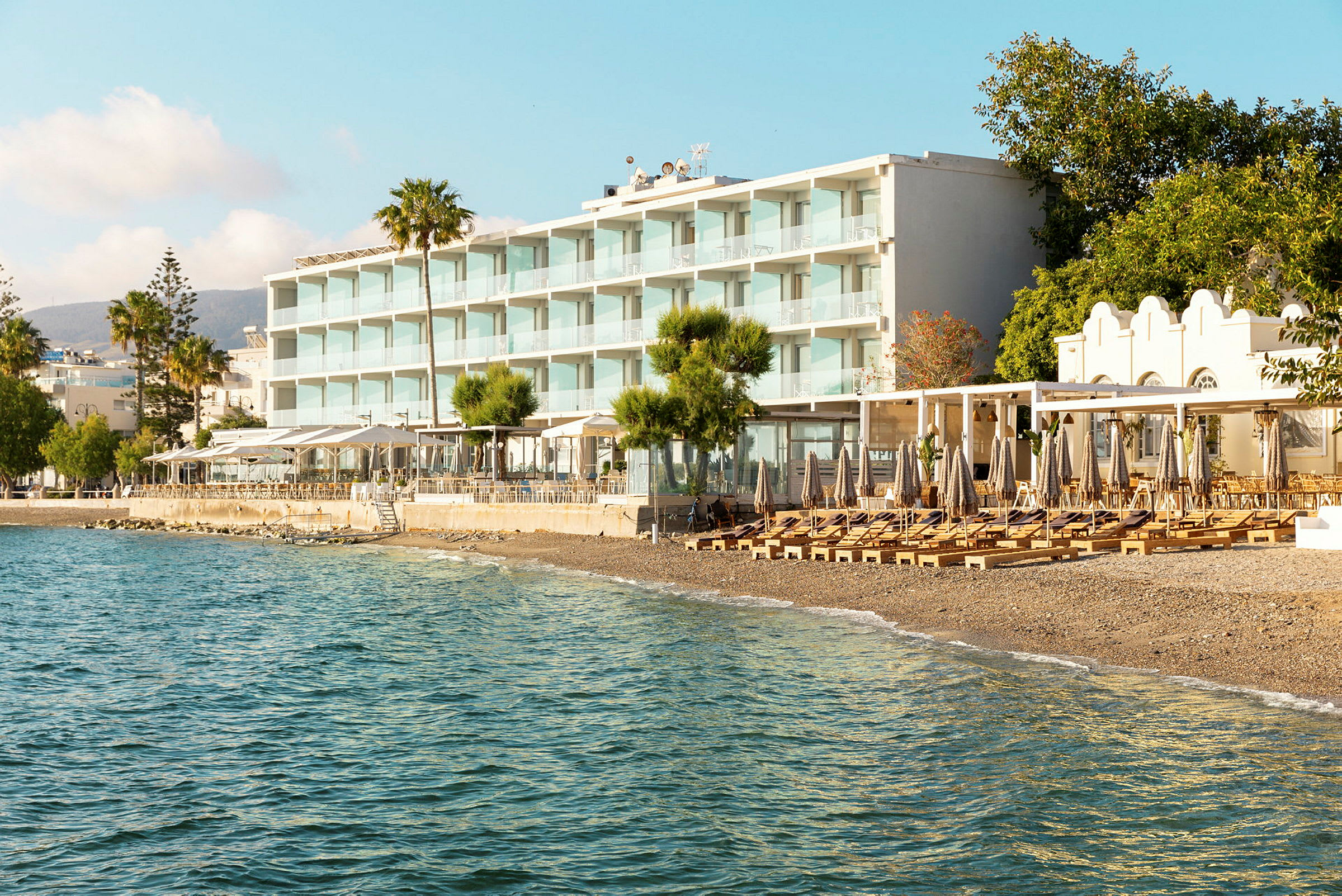 Udsigt til et strandhotel med liggestole og parasoller på stranden og havet i forgrunden. (AI-genereret tekst)