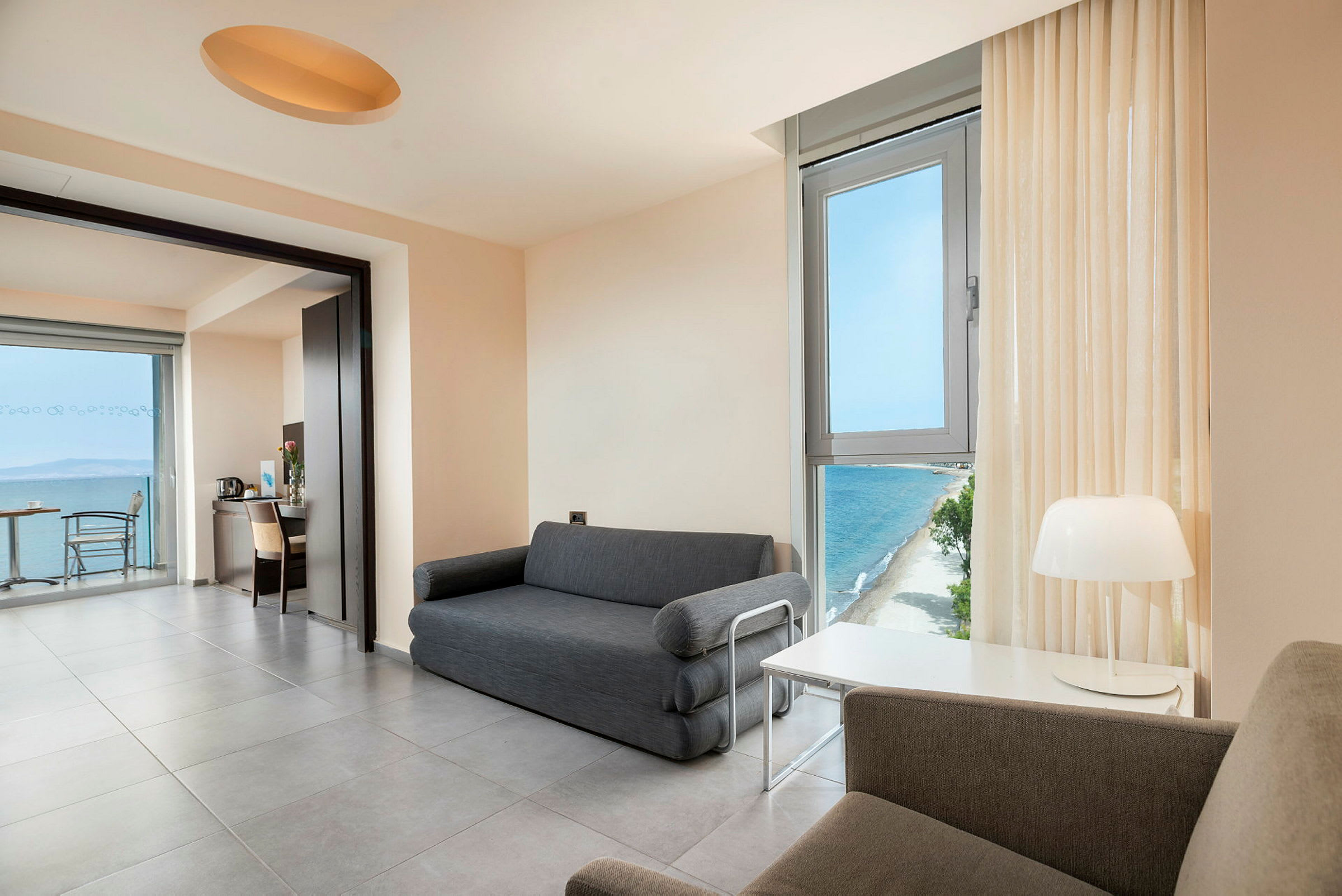 En moderne hotelsuit med siddearrangement, et bord, vindue med havudsigt og en lampe. (AI-genereret tekst)