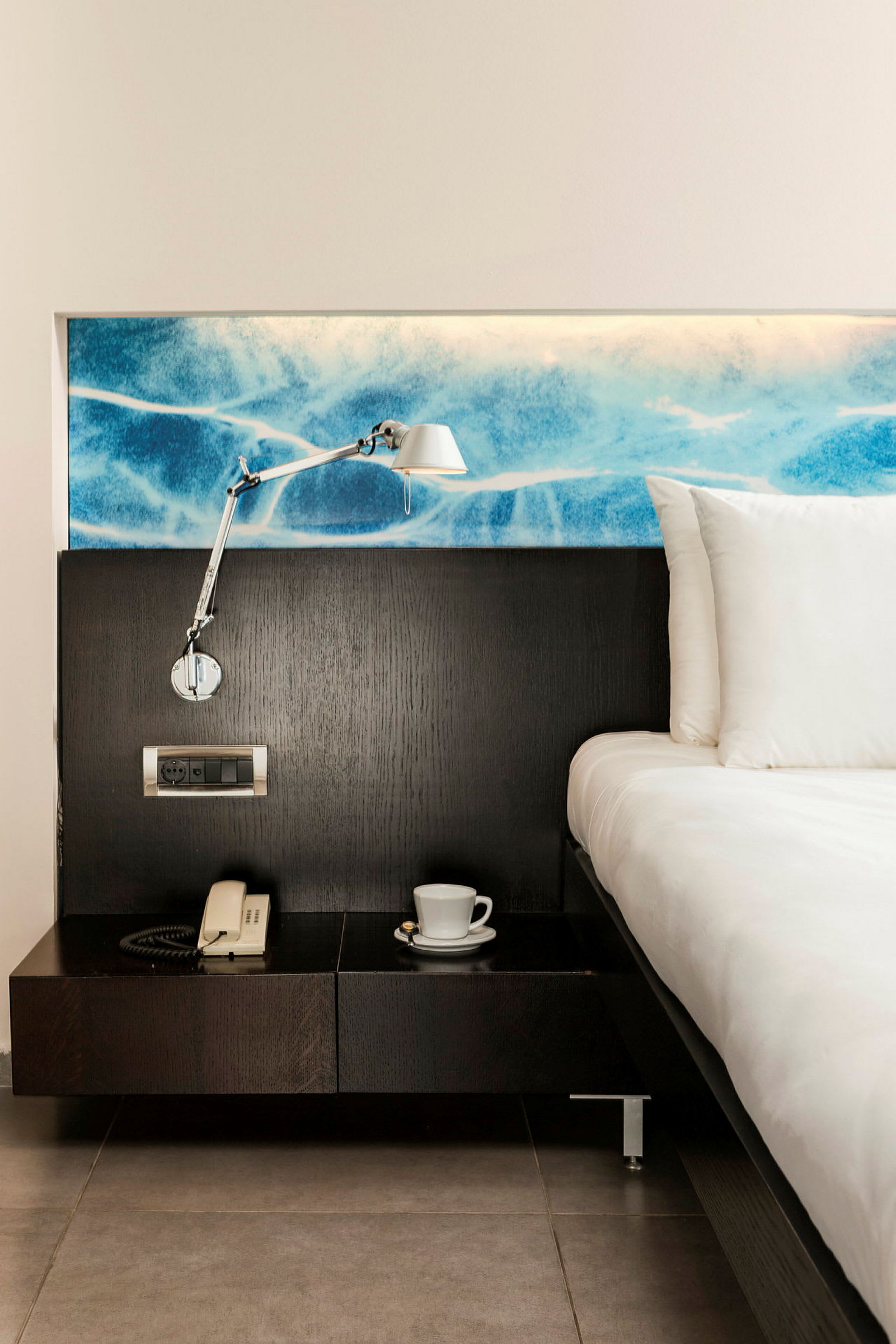 Hotelværelse med seng, natbord, lampe og telefon. (AI-genereret tekst)