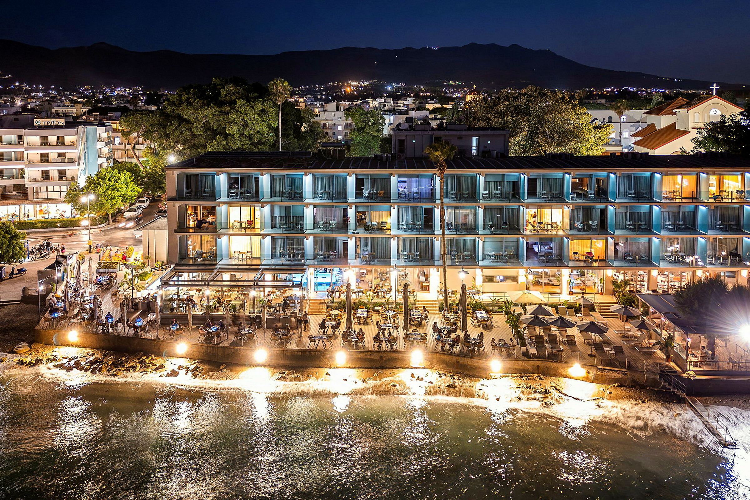 Hotelbygning og restaurant ved vandet, oplyst om aftenen. (AI-genereret tekst)